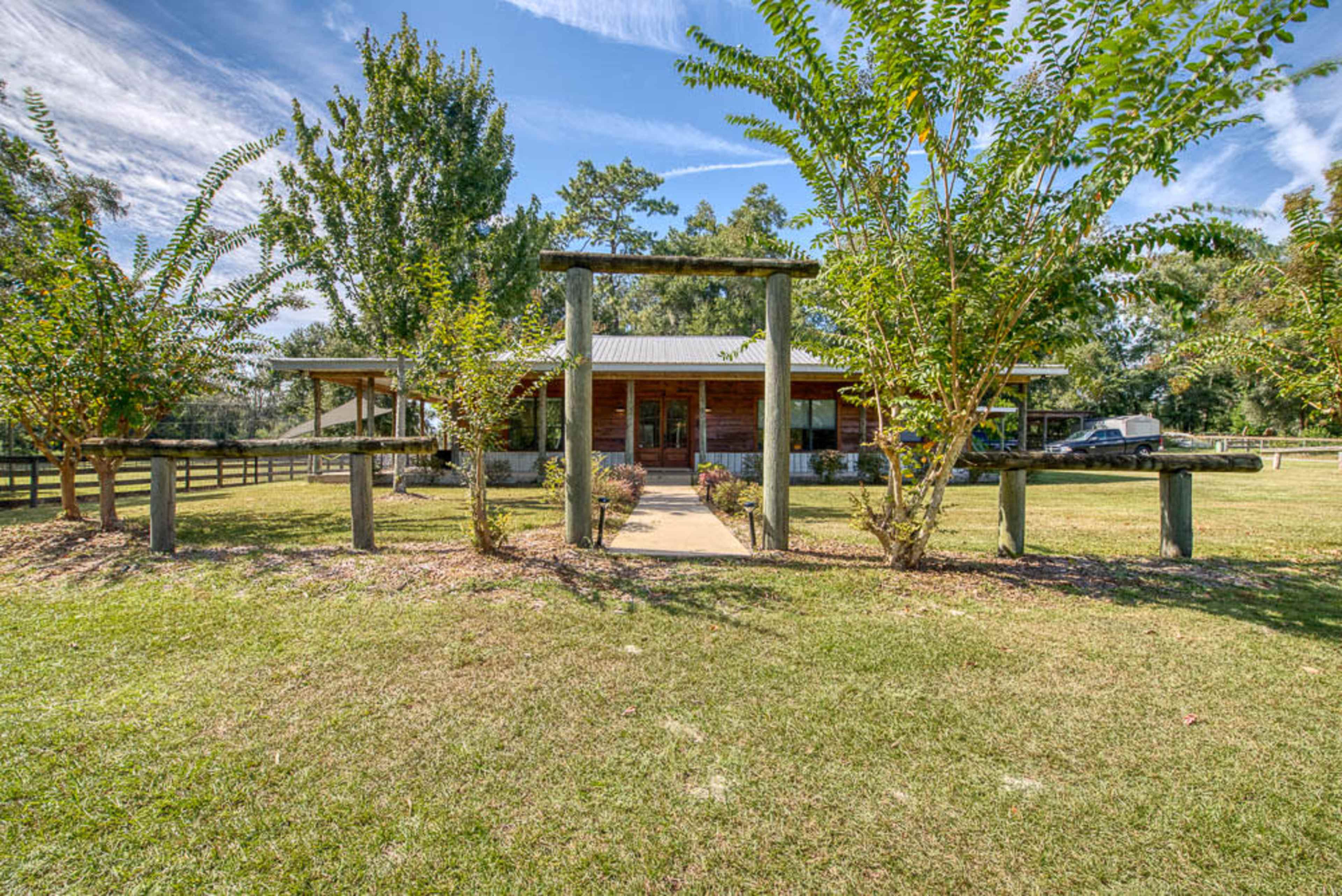 The image shows a wooden building surrounded by trees and a grassy area, with a pathway leading to the entrance.