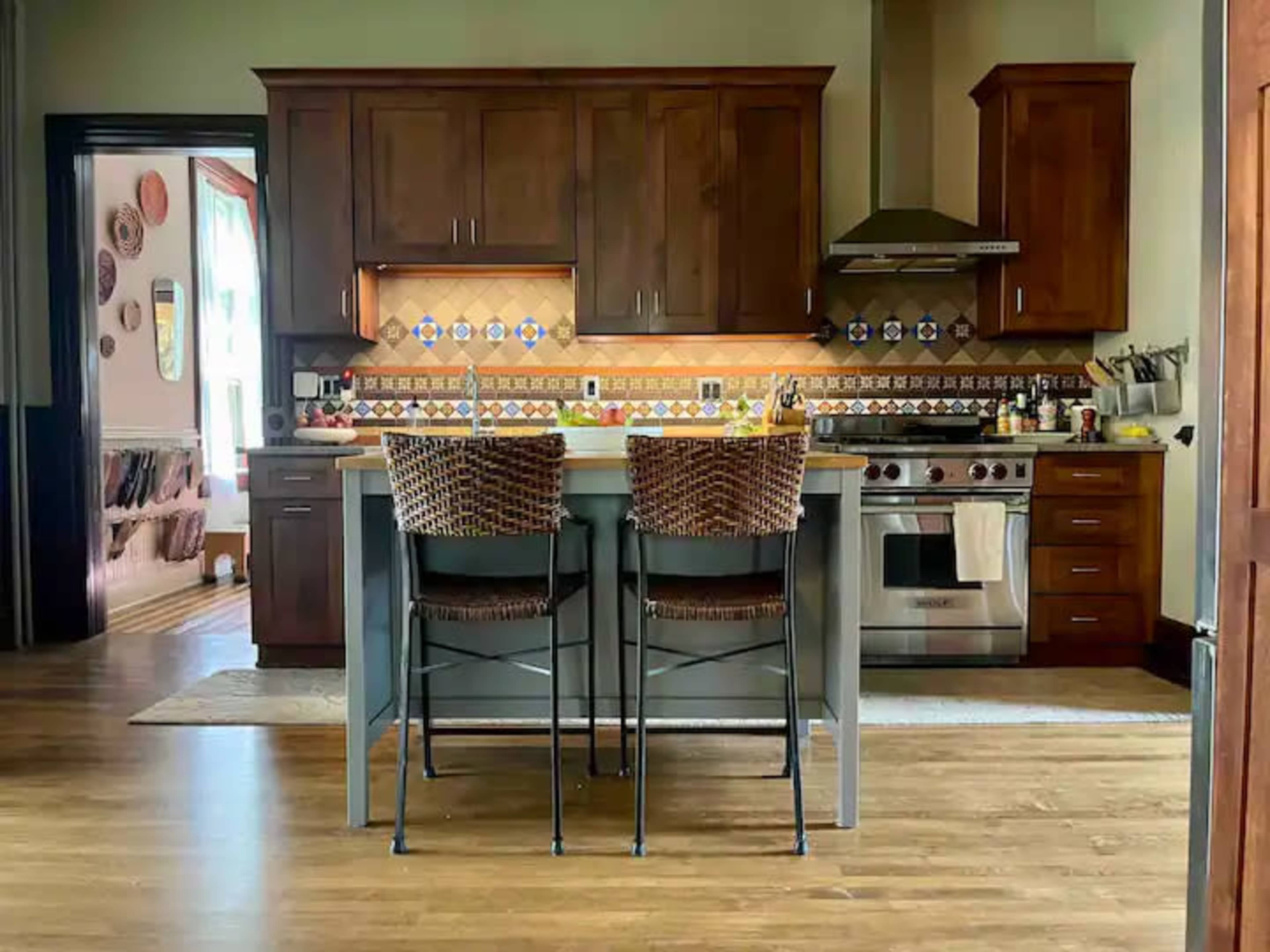 A kitchen with dark wood cabinets, a stainless steel gas range, and two woven bar stools at a central island.