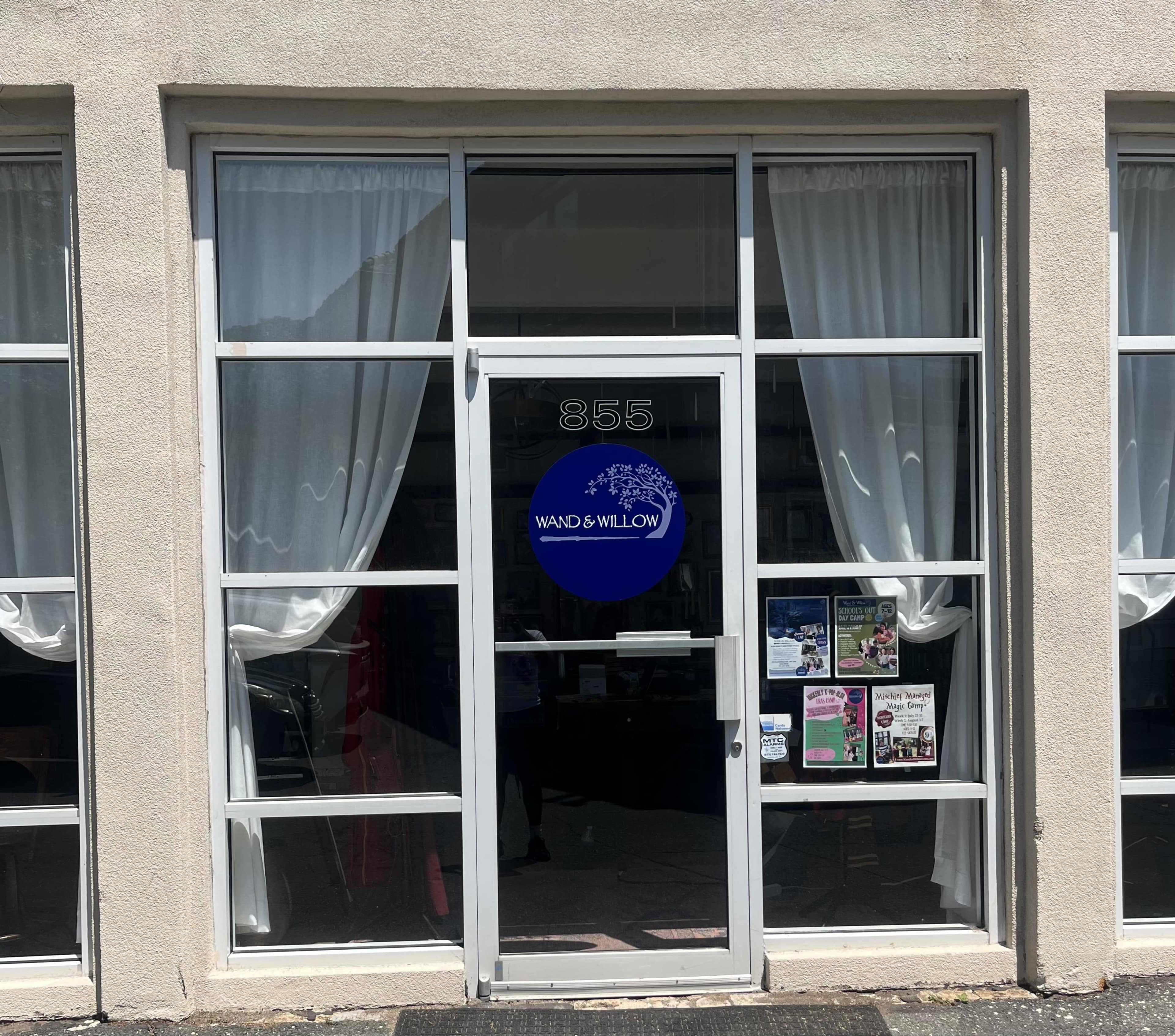 The storefront features large glass windows with sheer white curtains and a round blue sign that reads "WAND & WILLOW" at the entrance.