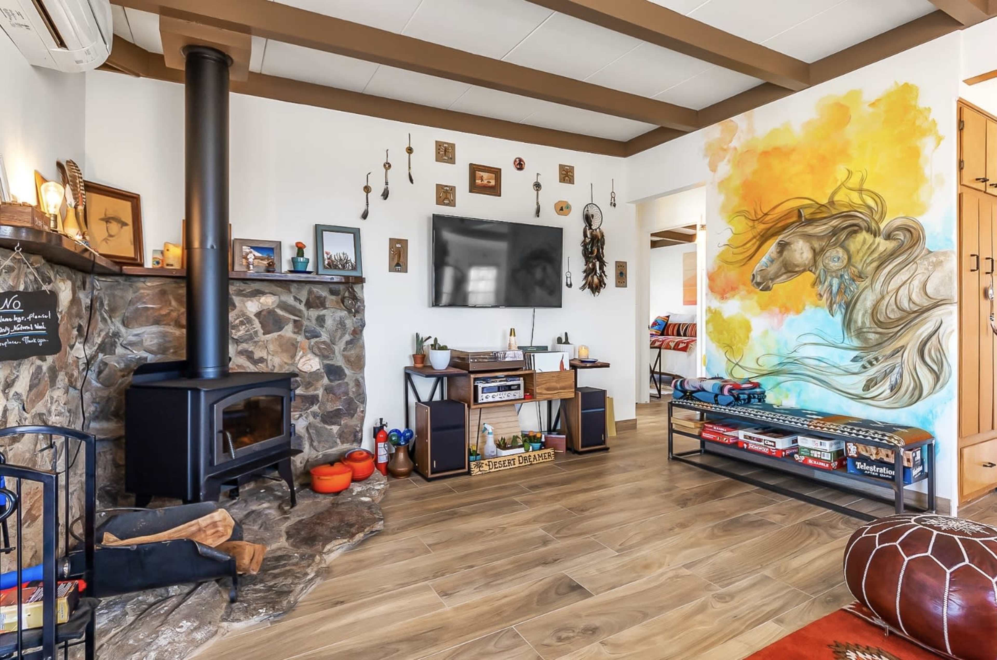 A living room featuring a wood stove with a stone facade, a TV on the wall, and a large mural of a horse.