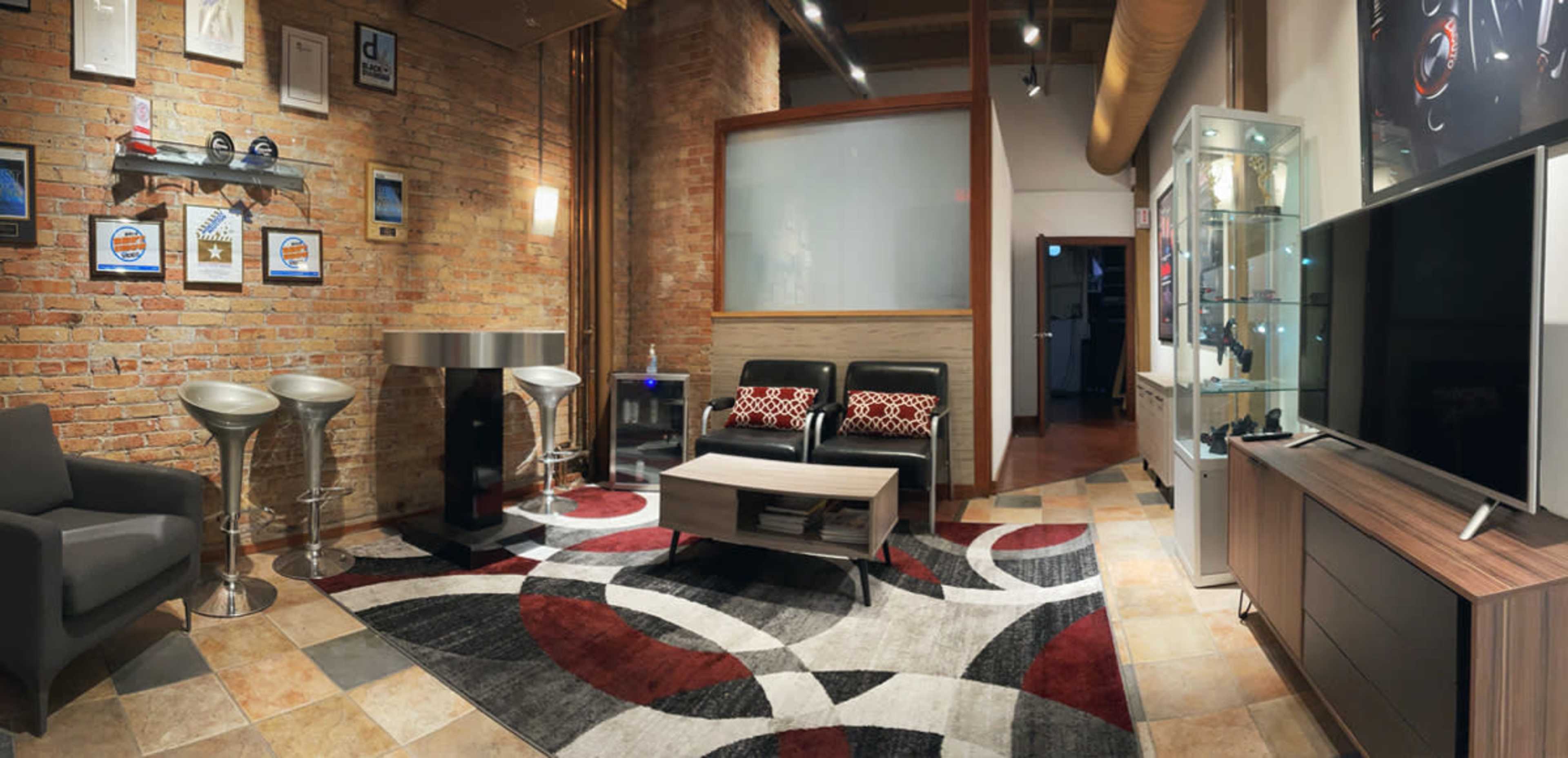 A modern interior space with exposed brick walls, stylish seating, a coffee table, a television, bar stools, and a display cabinet.