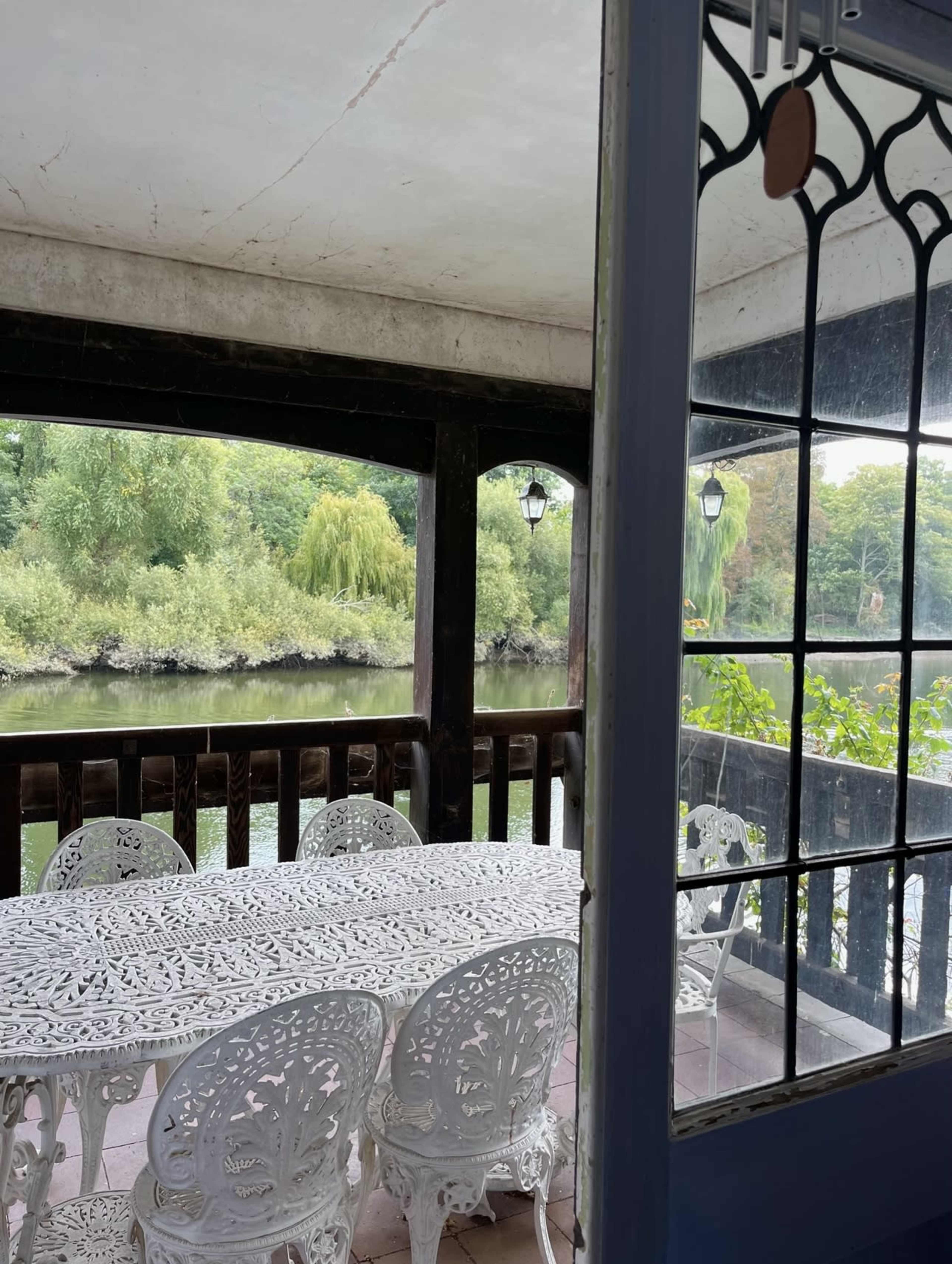 A white metal table and chairs are arranged on a porch overlooking a calm river surrounded by lush greenery.