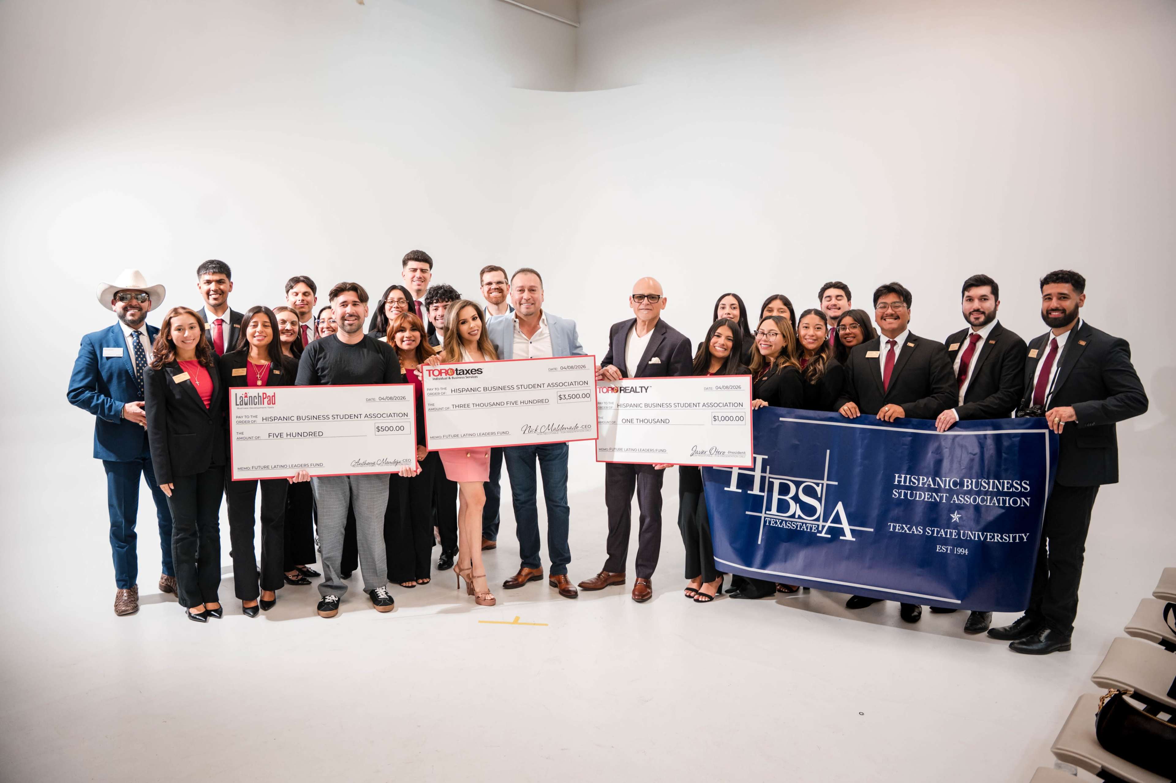 A large group of individuals stands together, holding oversized novelty checks and a banner representing the Hispanic Business Student Association at Texas Southern University.