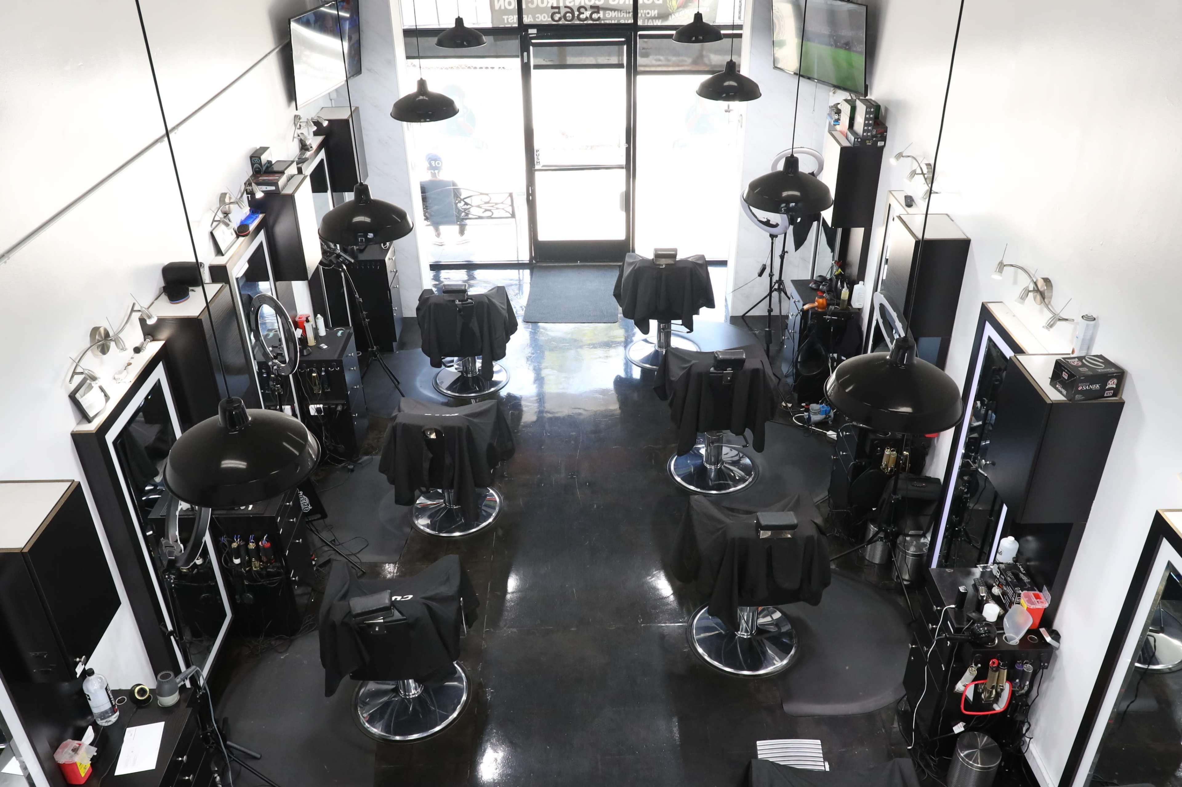 A hair salon interior with several styling stations, each featuring a black salon chair and lighting equipment, arranged in a spacious layout.