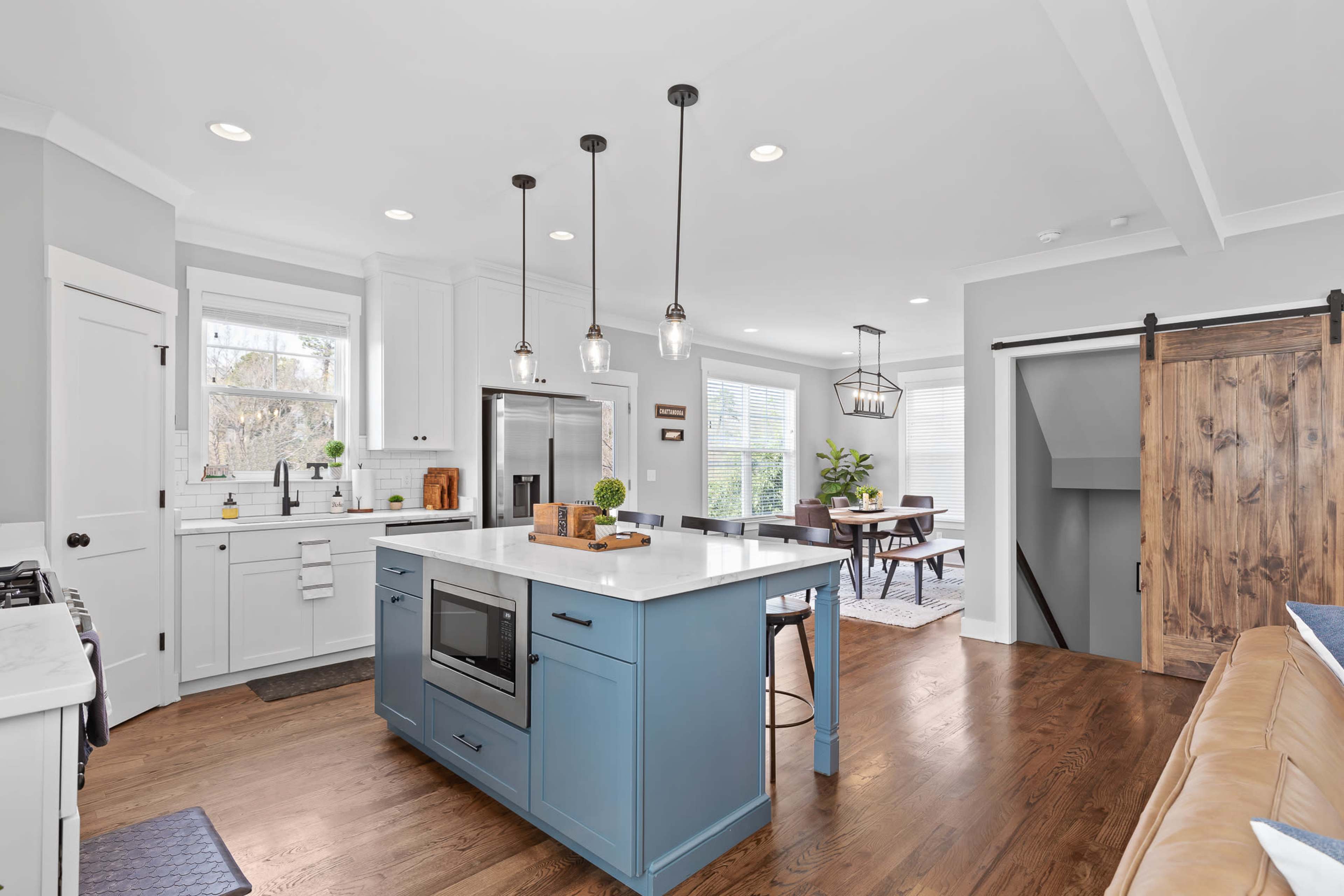 A modern kitchen features a central blue island with a white countertop, stainless steel appliances, and a sliding barn door leading to a staircase.
