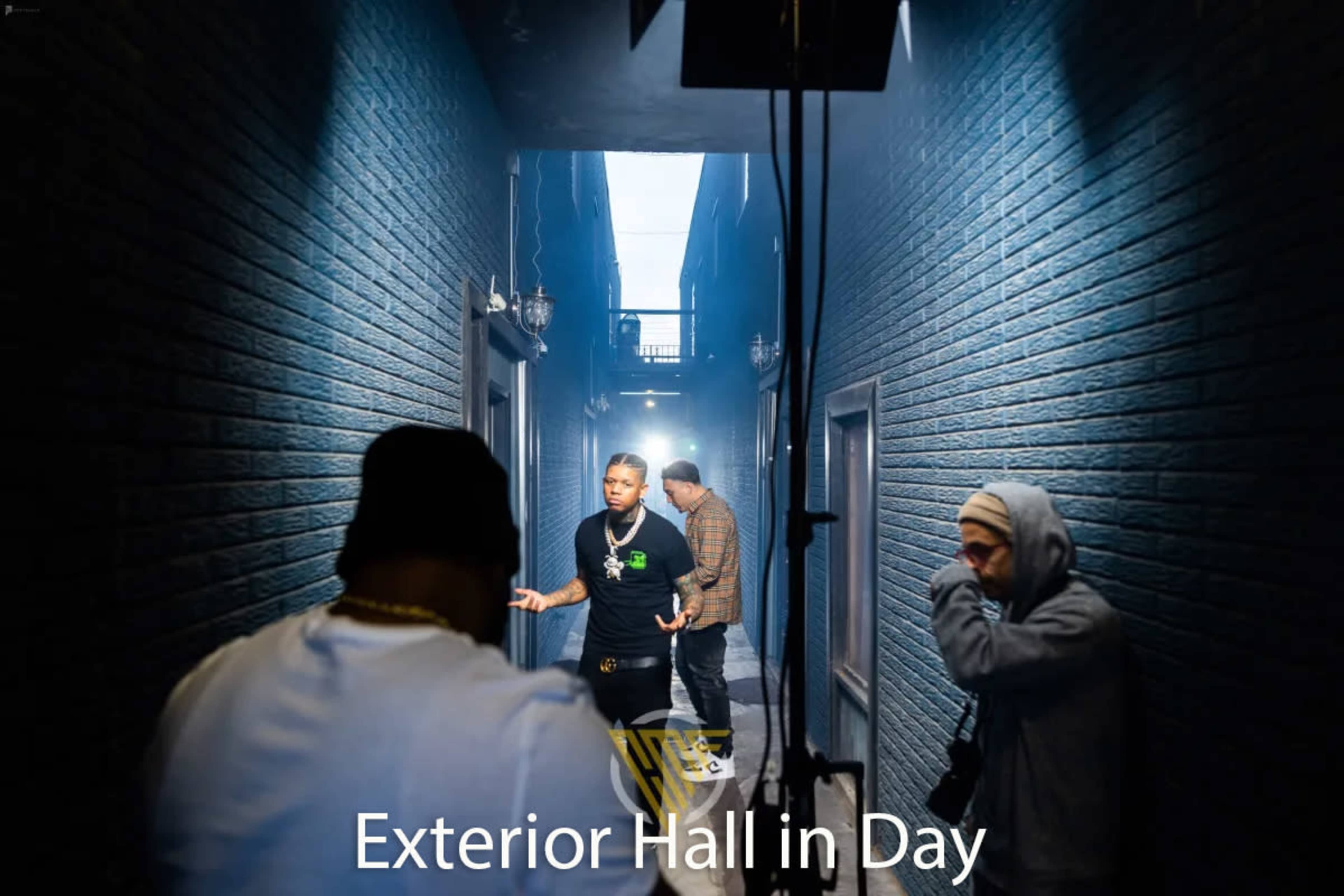 A group of musicians is filmed in a narrow, well-lit hallway with brick walls during the day.