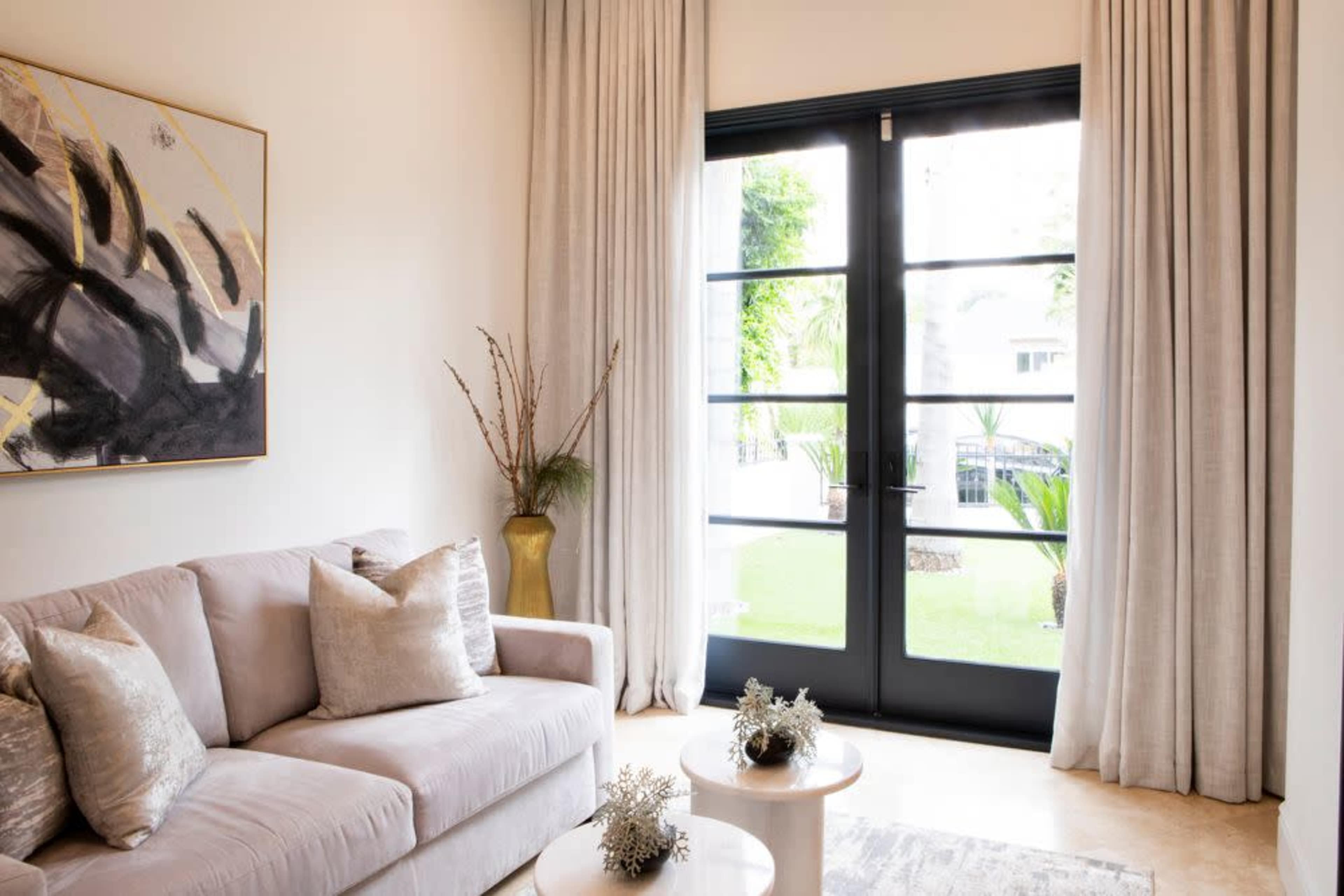 A modern living room with a gray sofa, two round coffee tables, and large glass doors opening to a garden area.