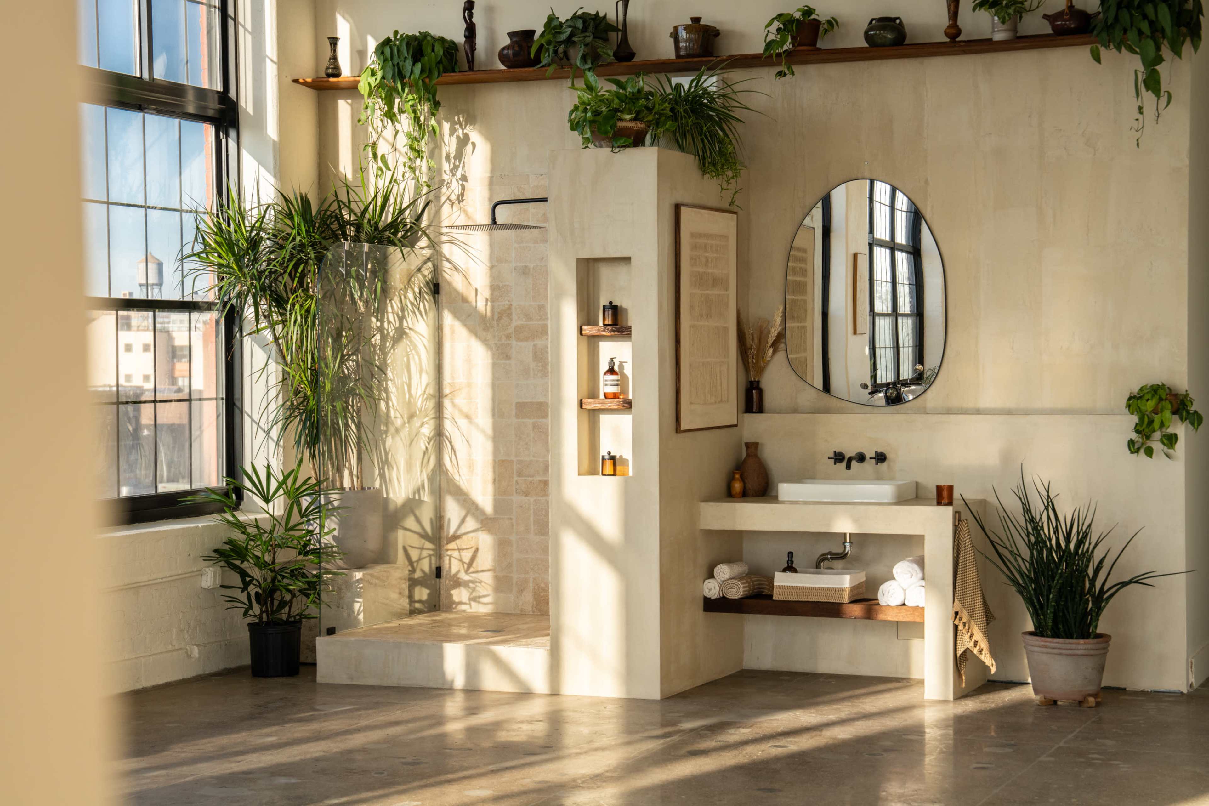 The image shows a bright bathroom featuring a tiled shower, a modern sink area, and various indoor plants against a light-colored wall.