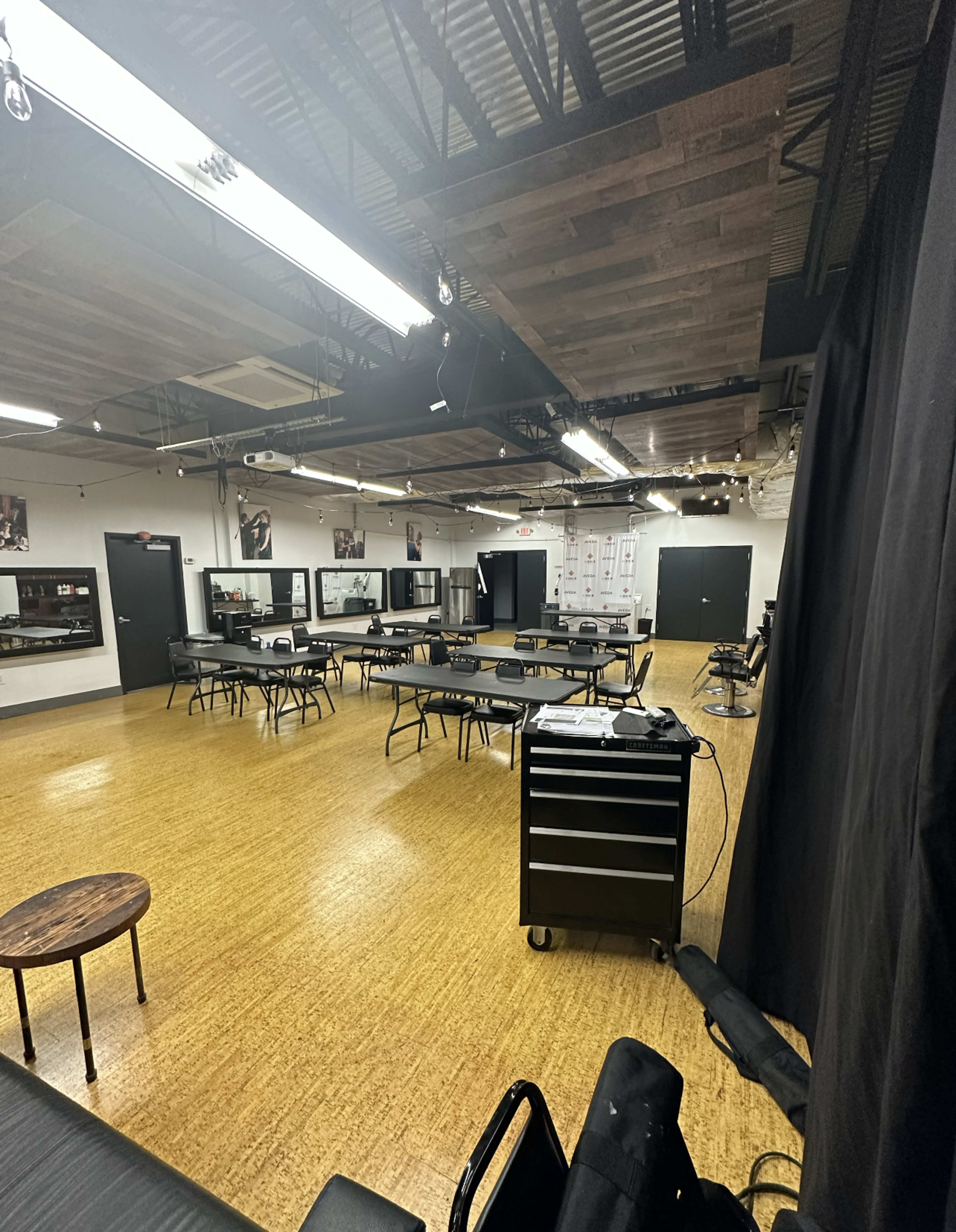 An empty studio space with multiple tables arranged in a grid, a workstation cabinet, and black curtains along one side.