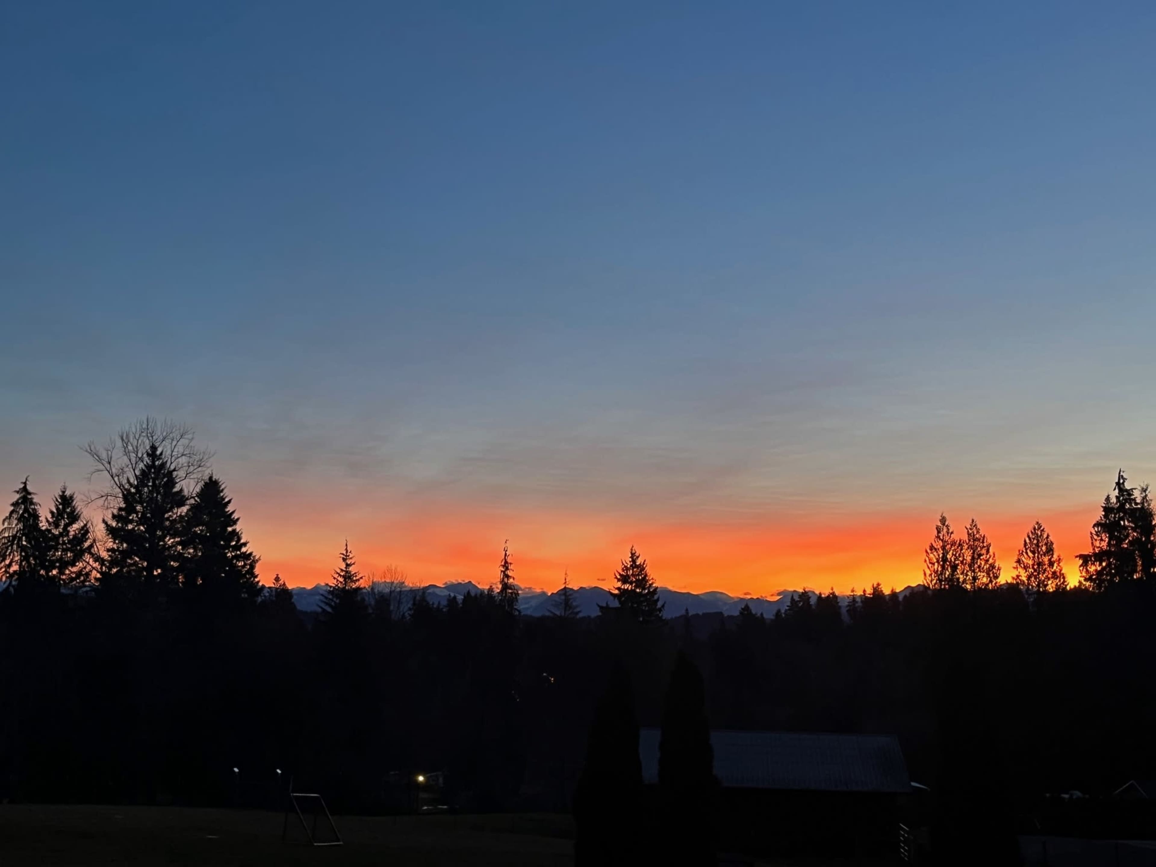 The image shows a sunset over a mountainous horizon with silhouetted trees and a clear sky transitioning from blue to orange.