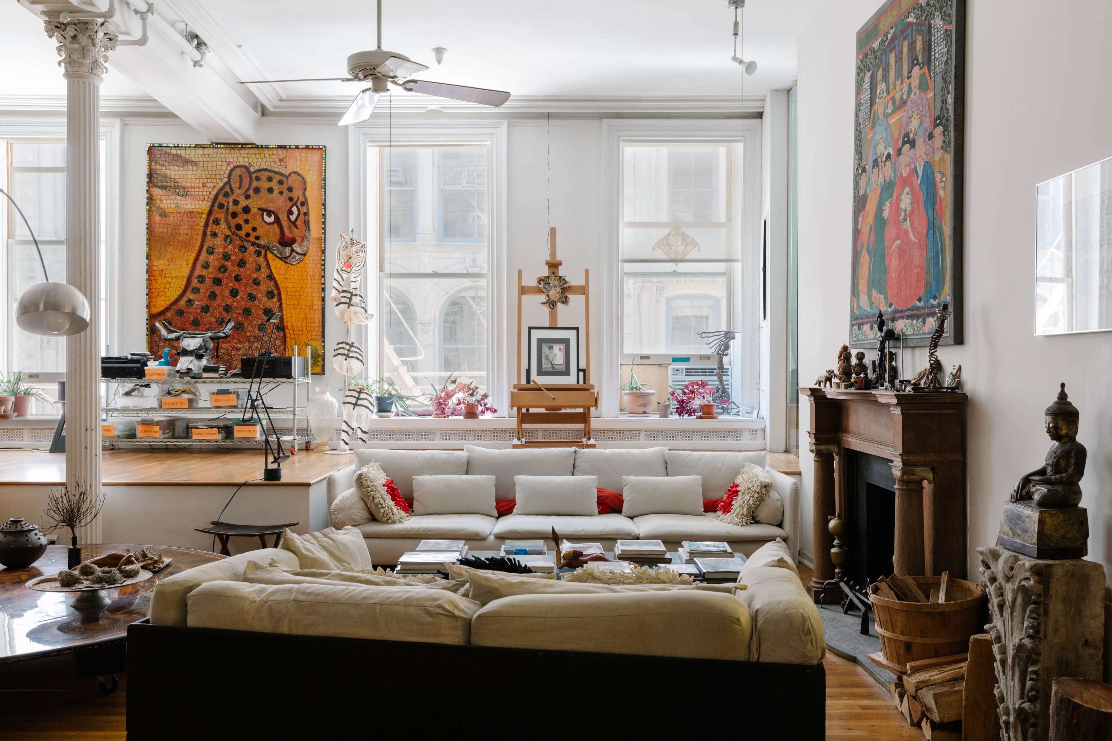 A spacious living room featuring a large sectional sofa, a wooden dining area with art displayed on the walls, and a mix of decorative items, including sculptures and plants.
