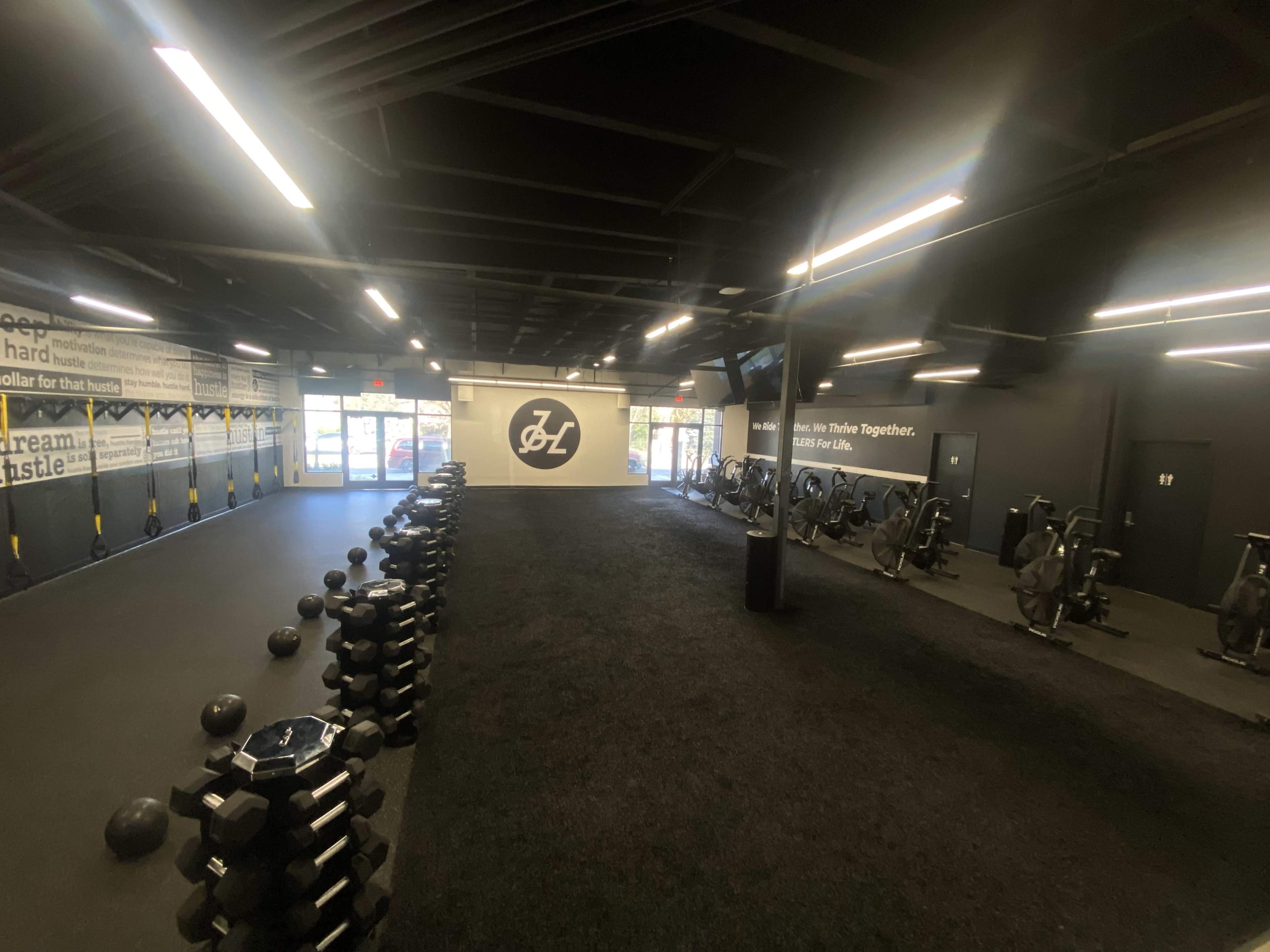 A fitness gym with rows of kettlebells on one side and exercise bikes lined against the wall, featuring motivational posters.