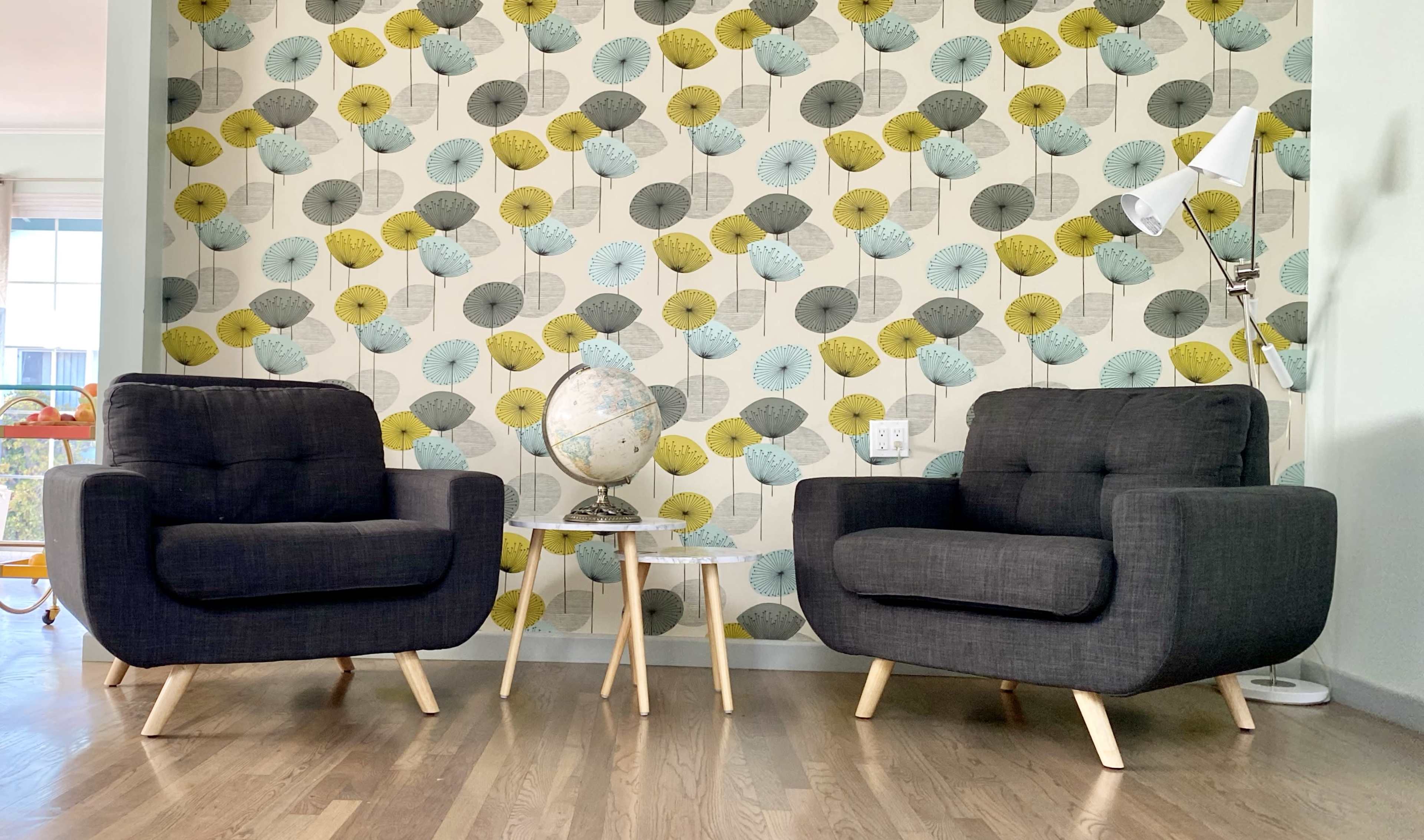 The image shows two gray armchairs positioned facing each other with a small table and a globe between them, set against a wallpaper decorated with colorful leaf patterns.