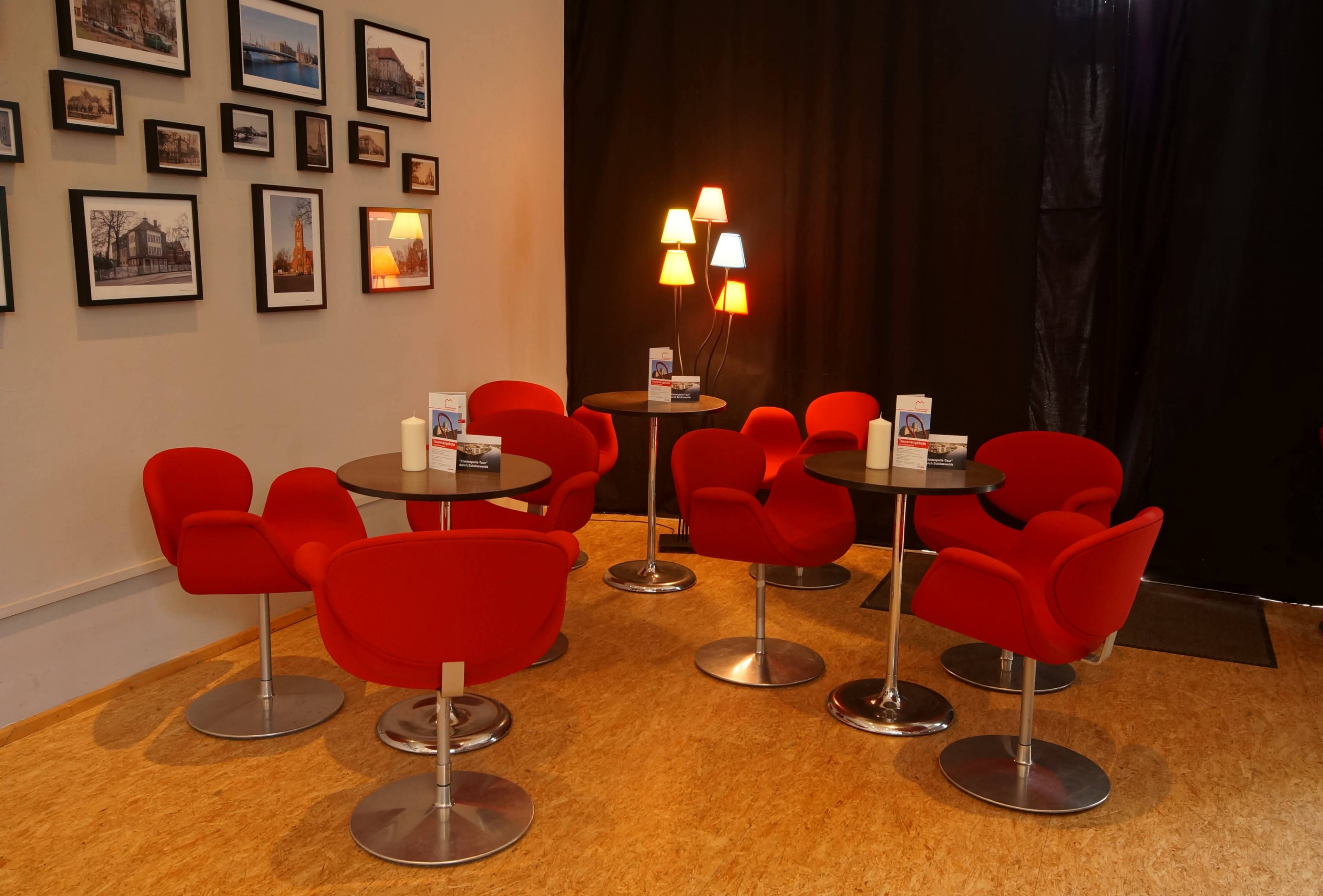 The scene features a cozy seating area with red chairs and round tables, illuminated by a multicolored lamp against a black backdrop.