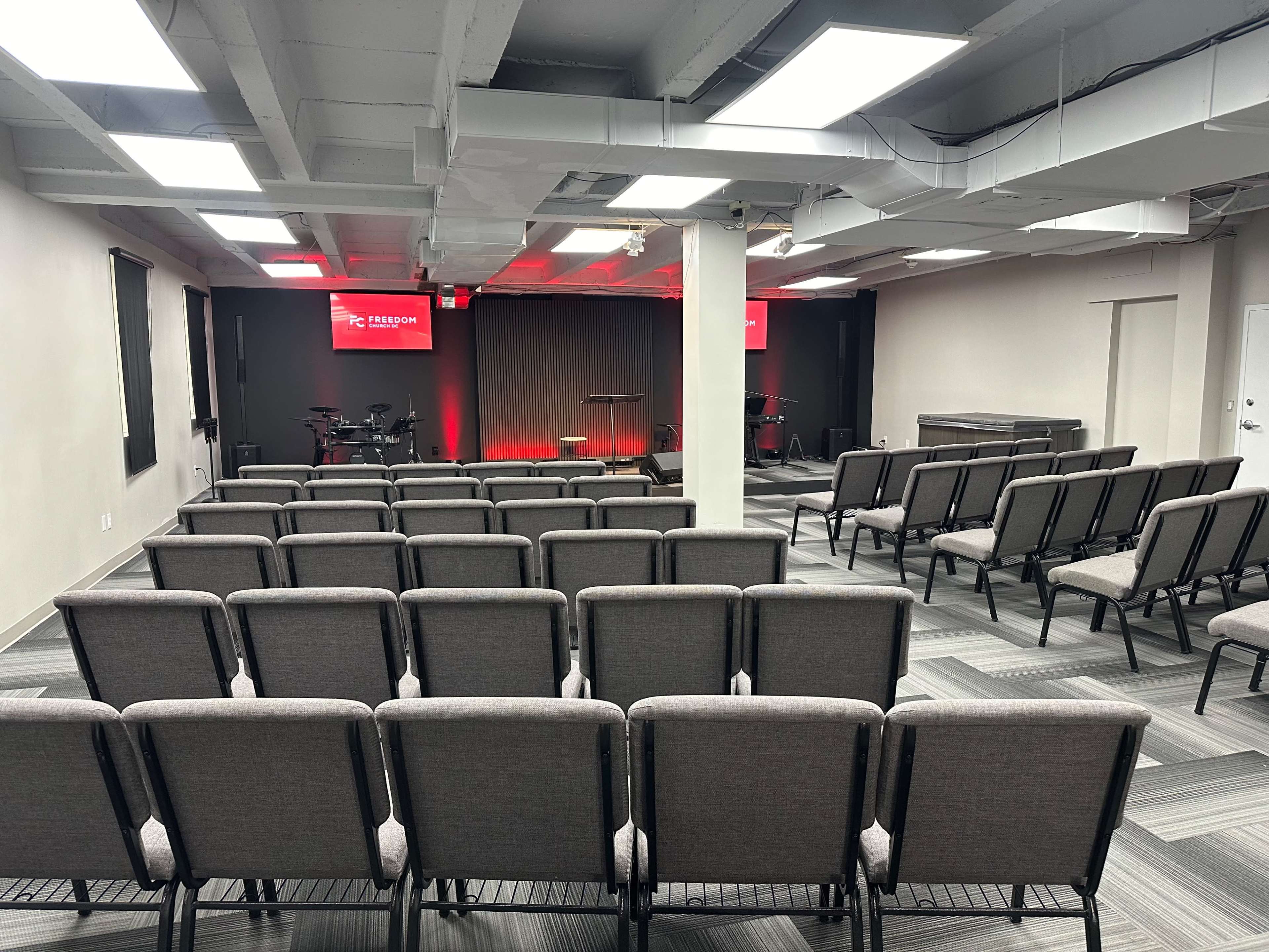 The image shows an organized meeting space with rows of chairs facing a small stage, illuminated by red lights in the background.