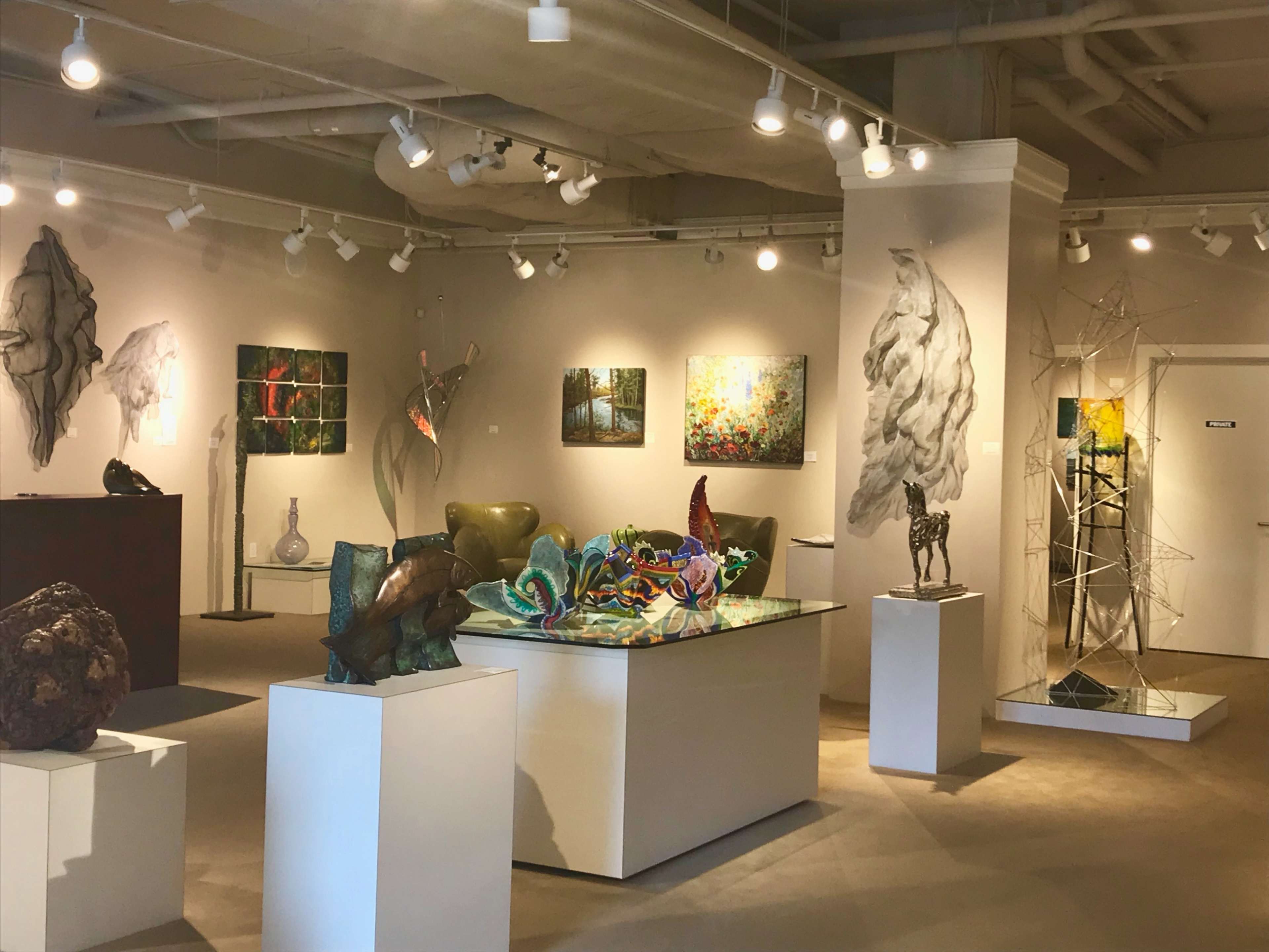 A modern art gallery featuring various sculptures and paintings displayed on the walls and pedestals.