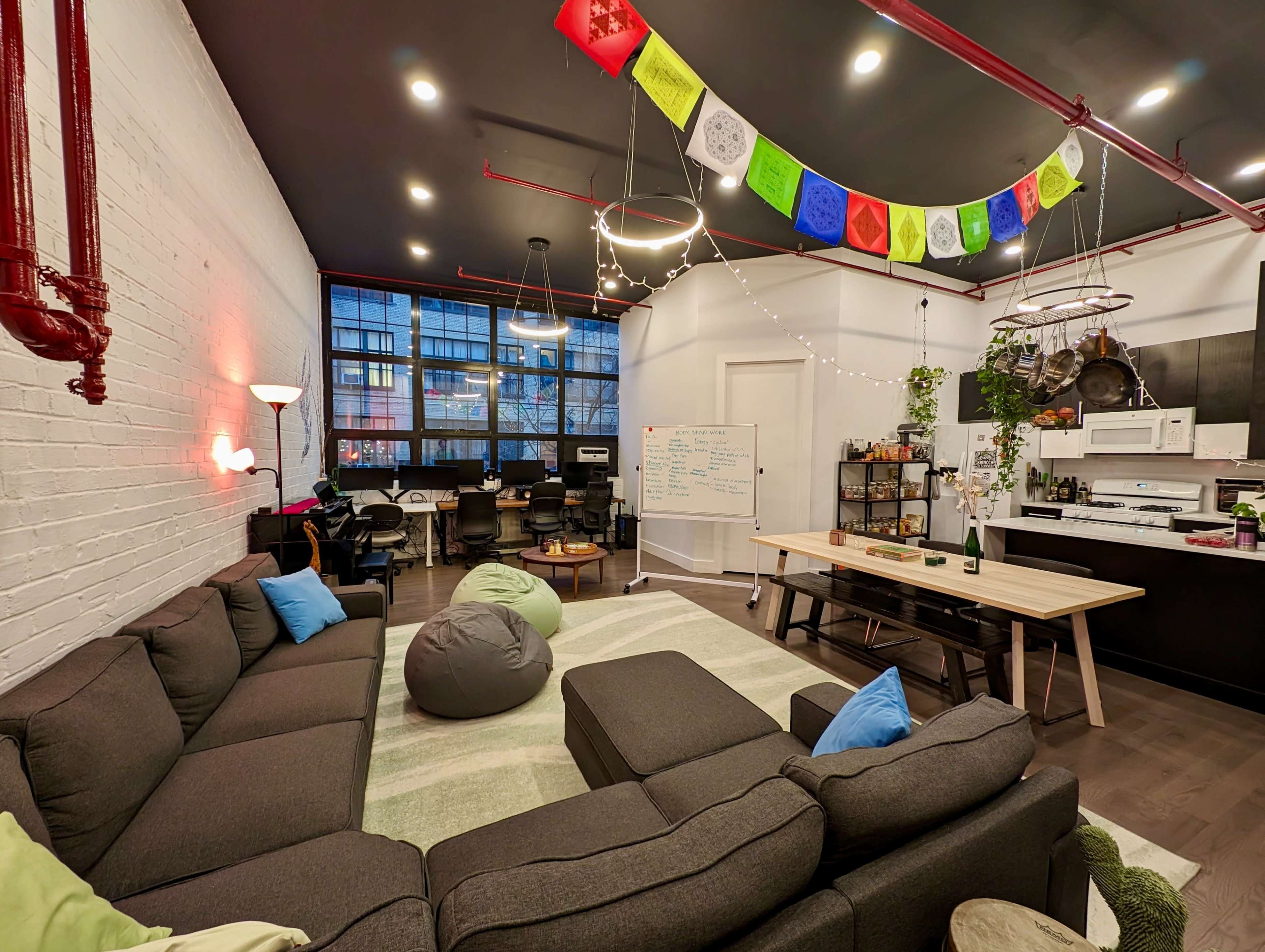 A modern, open office space with a sectional sofa, bean bags, a long dining table, and colorful banners hanging from the ceiling.