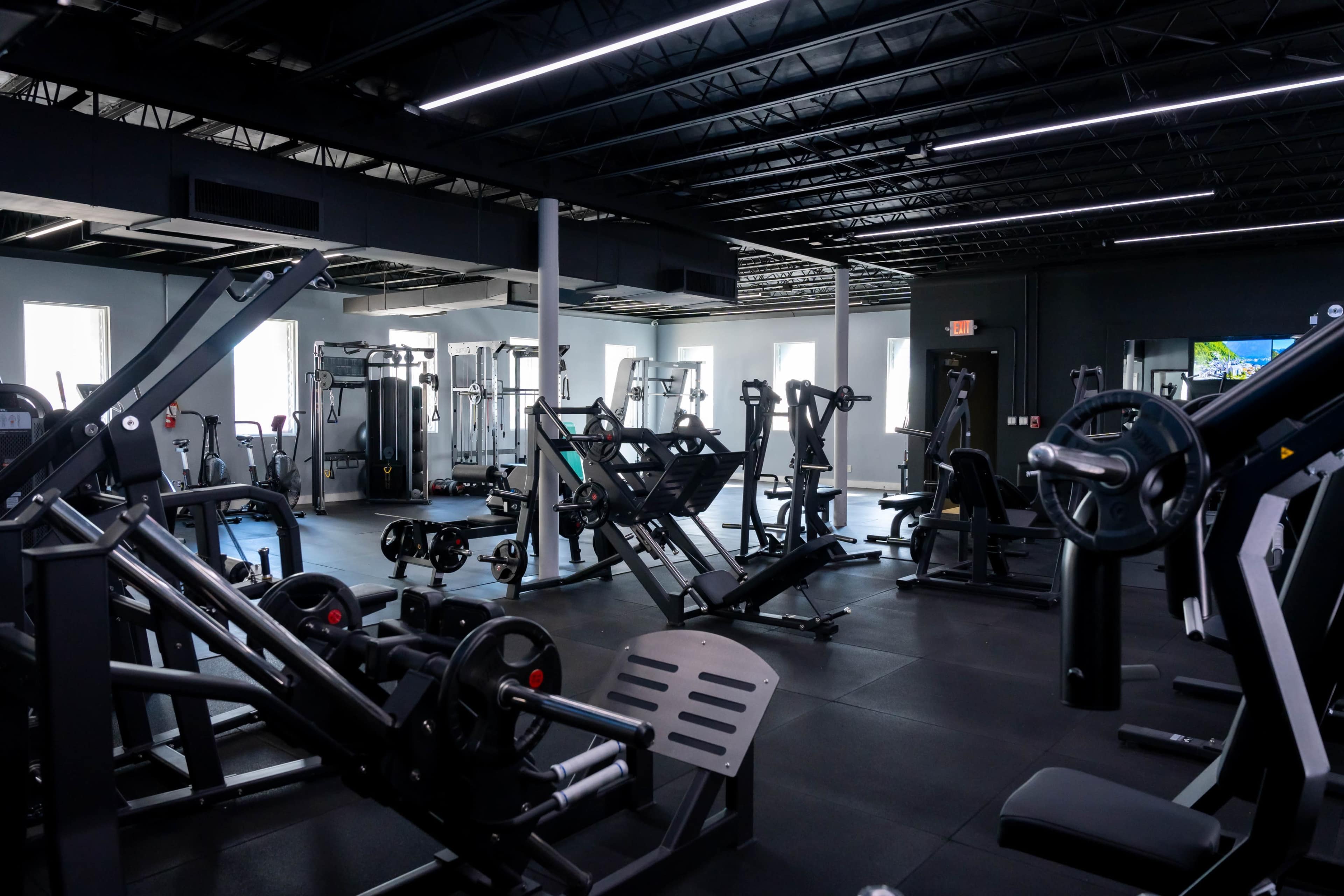 The image shows a modern gym interior filled with various exercise machines and equipment arranged throughout the space.