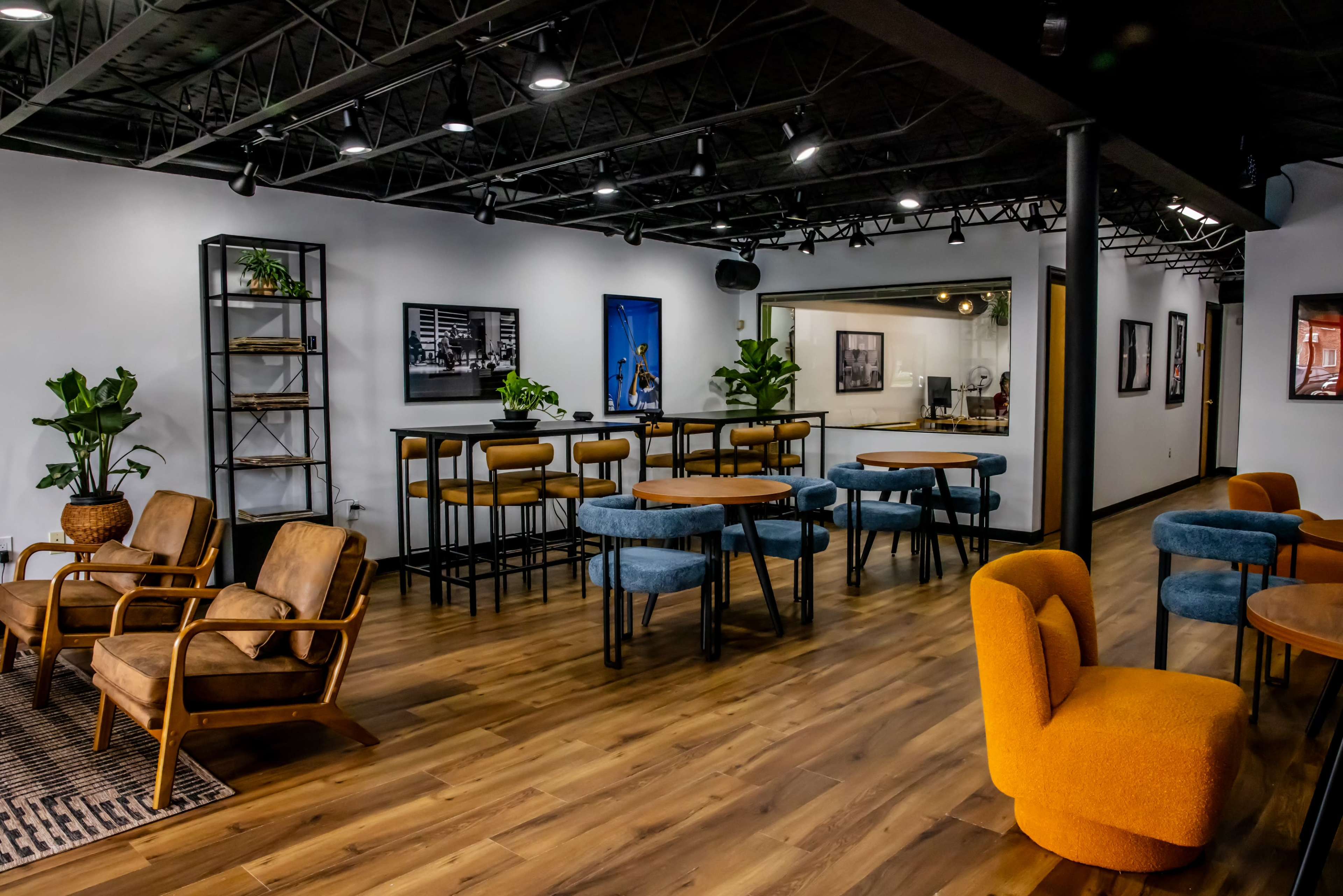 A modern lounge area featuring various seating arrangements, including armchairs and tables, surrounded by plants and artwork on the walls.