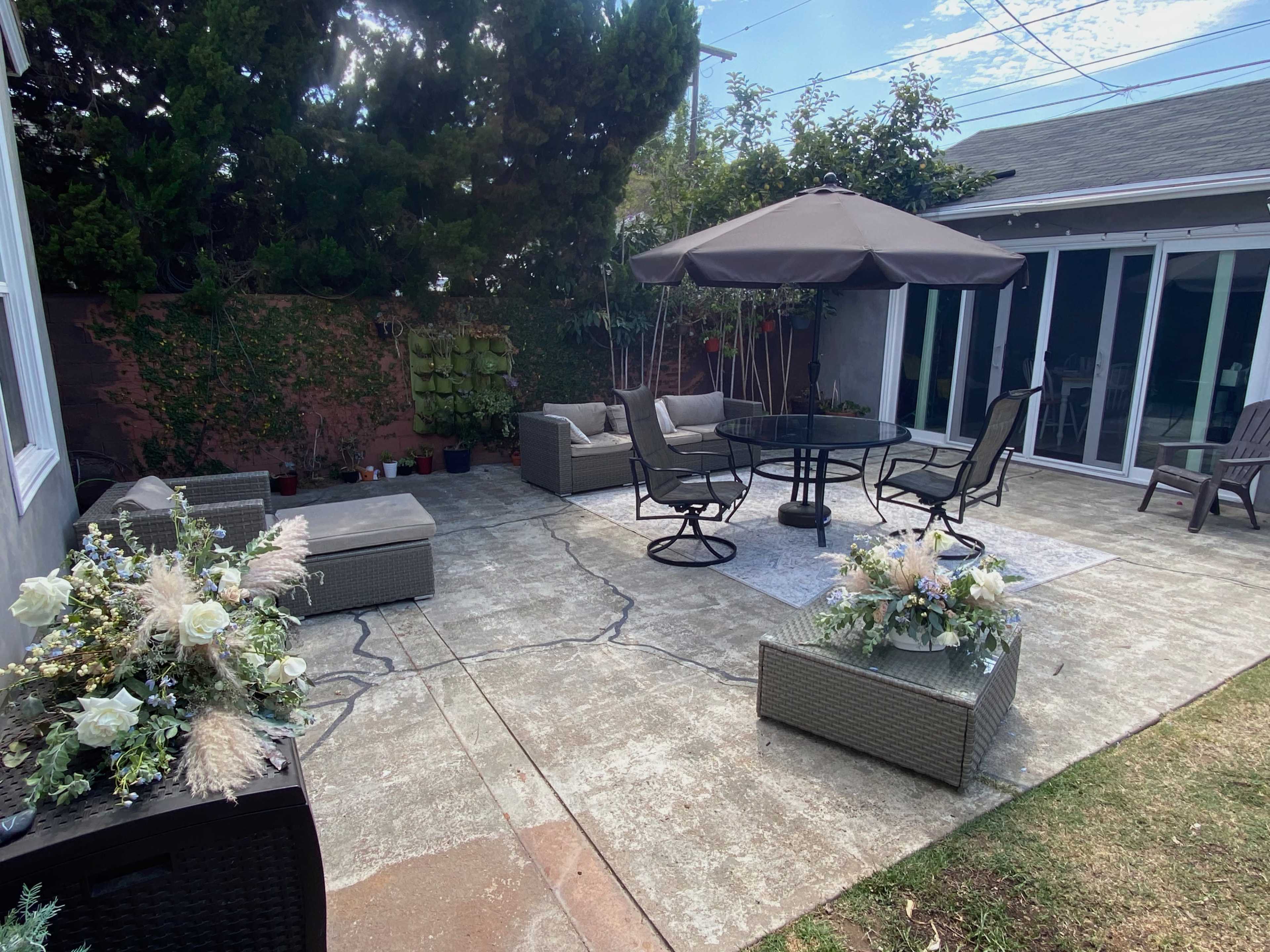 A patio area with outdoor furniture, including a dining table and chairs, an umbrella for shade, and decorative planters.