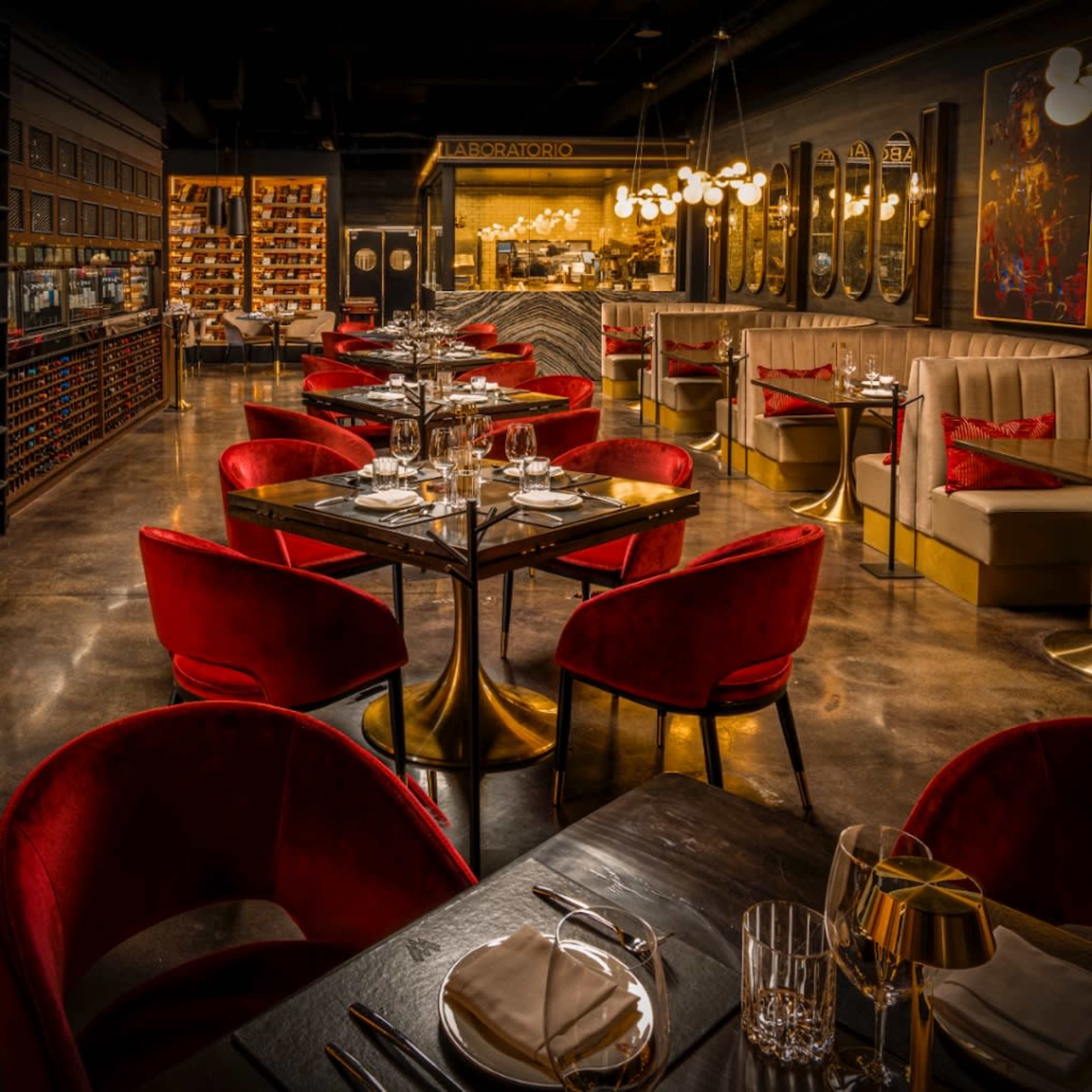 The image shows a modern restaurant with elegant red chairs and tables set for dining, featuring a stylish interior design with warm lighting and decorative elements.