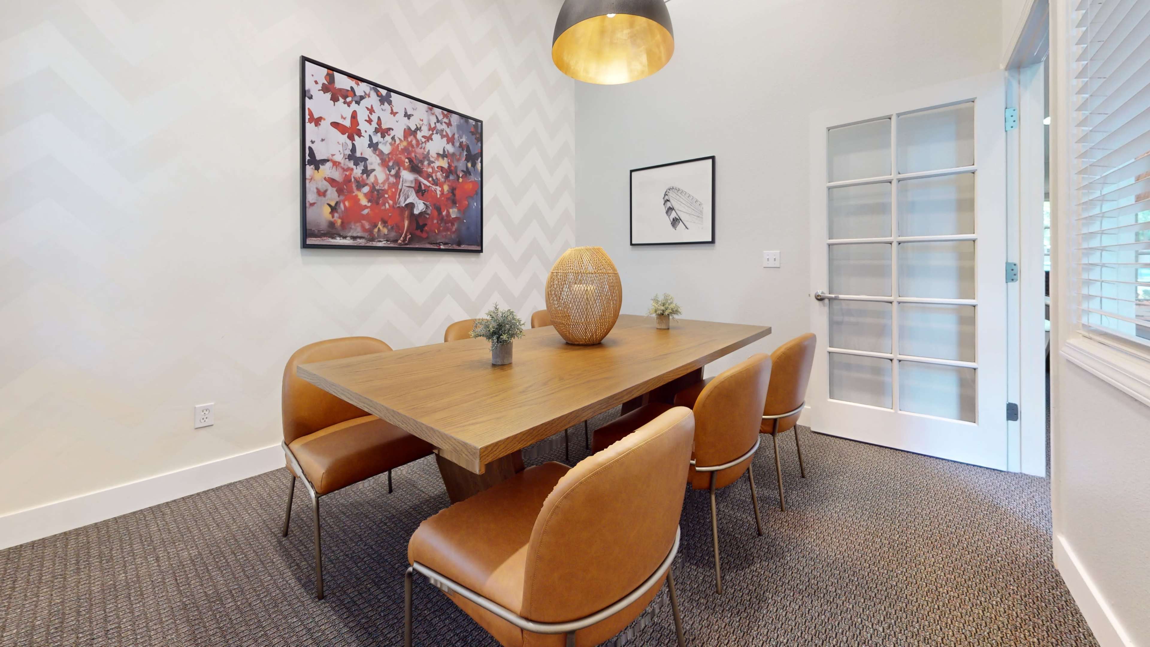 A modern dining room features a wooden table surrounded by six leather chairs, a large decorative vase, and vibrant artwork on the walls.