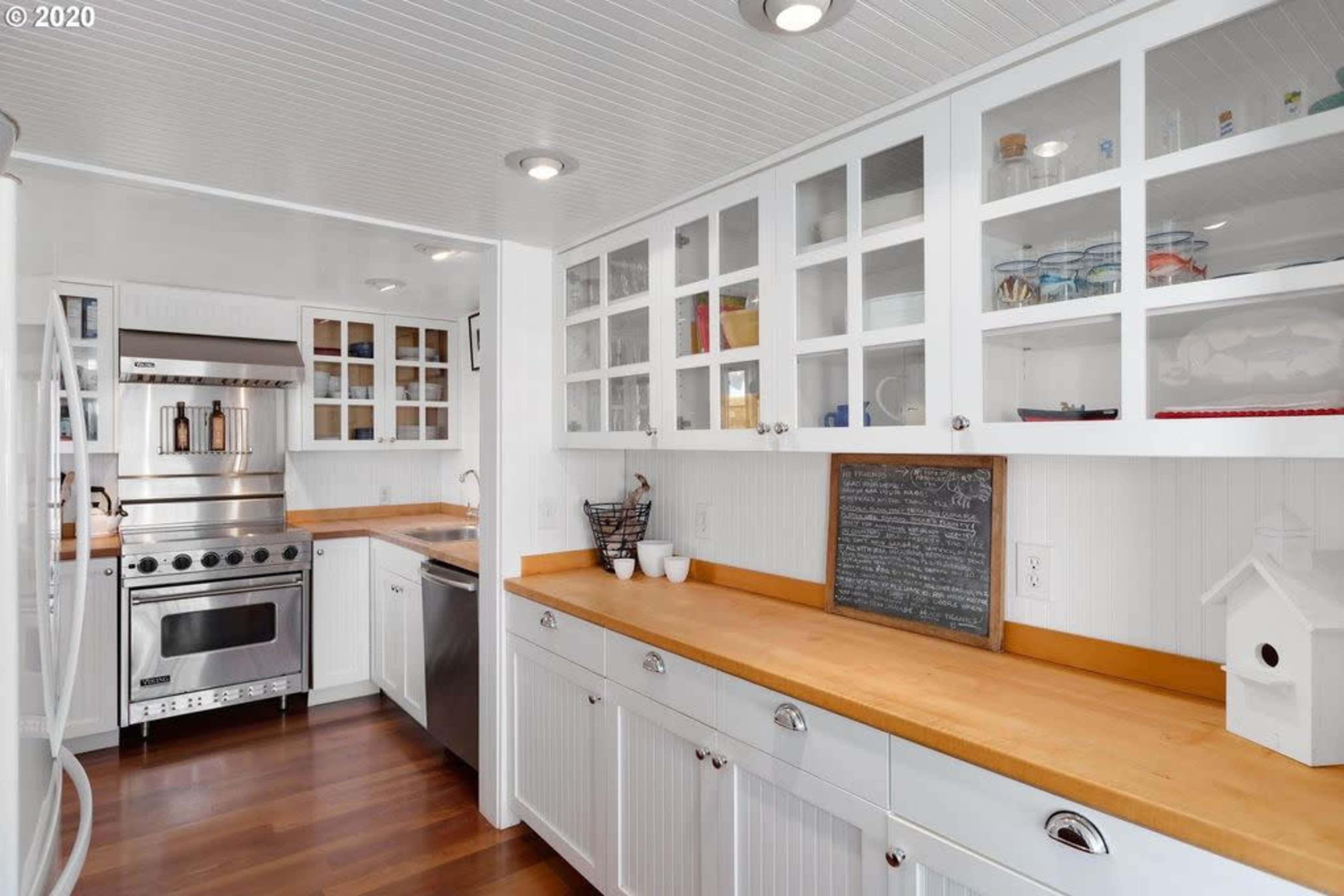 The image shows a modern kitchen with white cabinetry, stainless steel appliances, and wooden countertops.