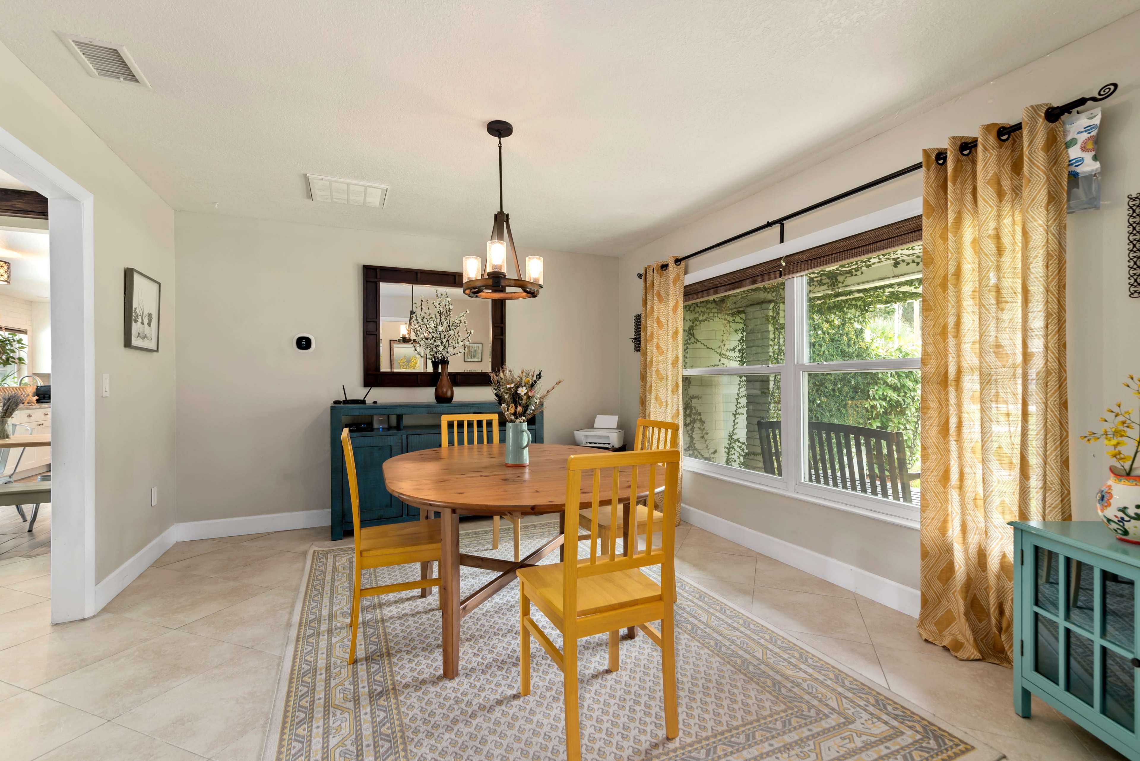 The dining area features a round wooden table with four yellow chairs, surrounded by windows that let in natural light.