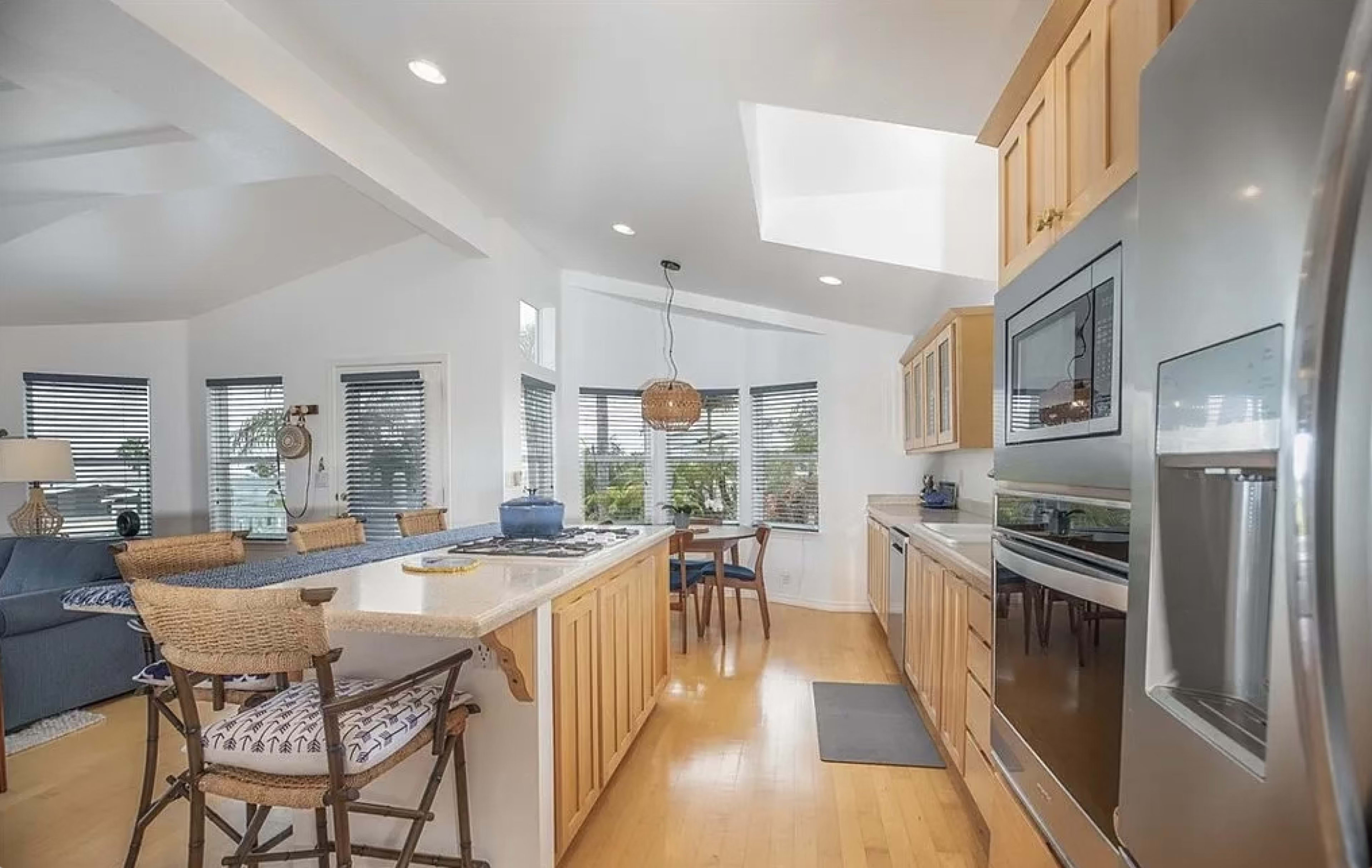 A modern kitchen with wooden cabinets, a large island with seating, and a bright, open layout featuring multiple windows.