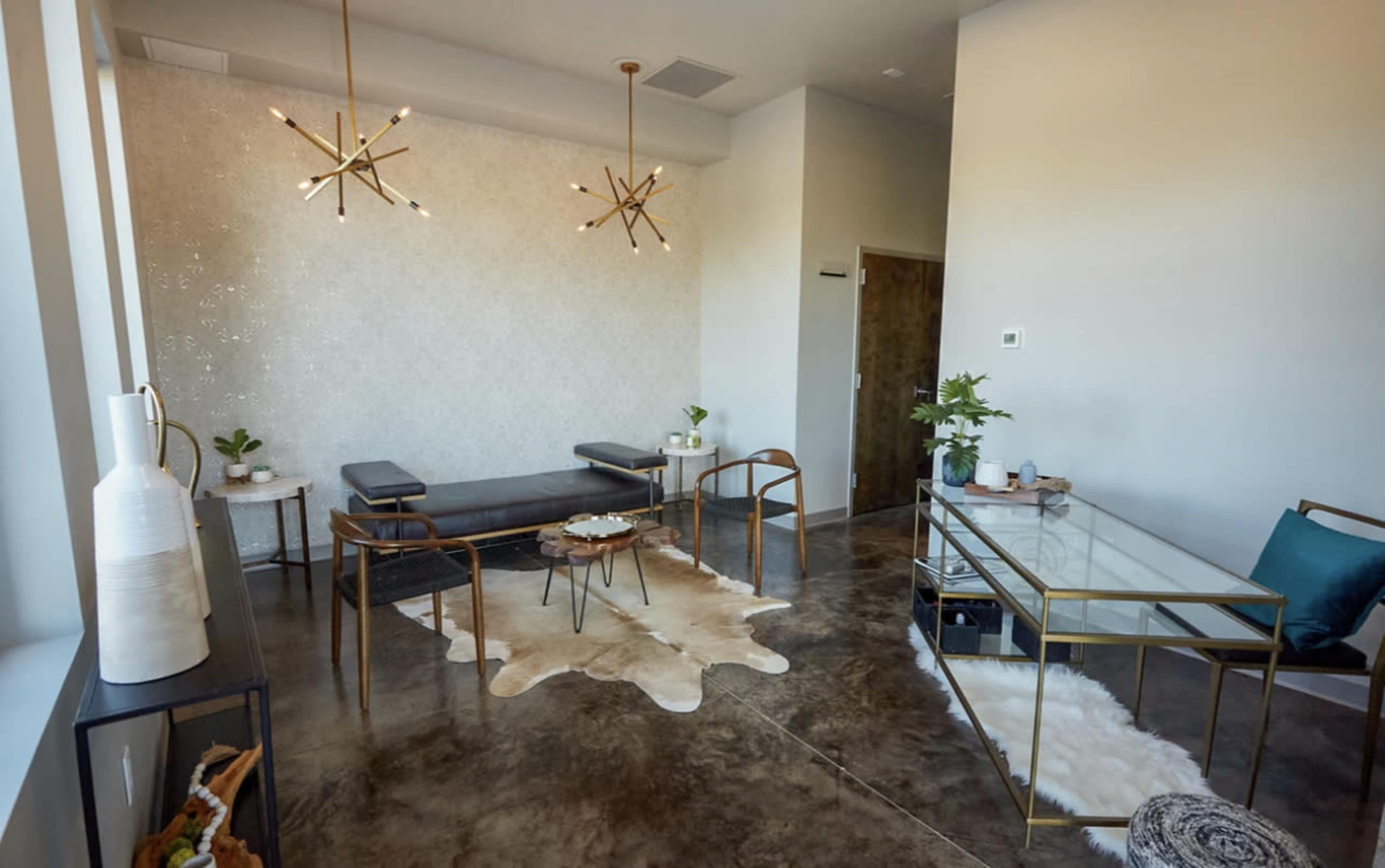 A modern interior space featuring a seating area with a leather bench, a glass coffee table, and decorative plants, all set against a textured wall and polished concrete floor.