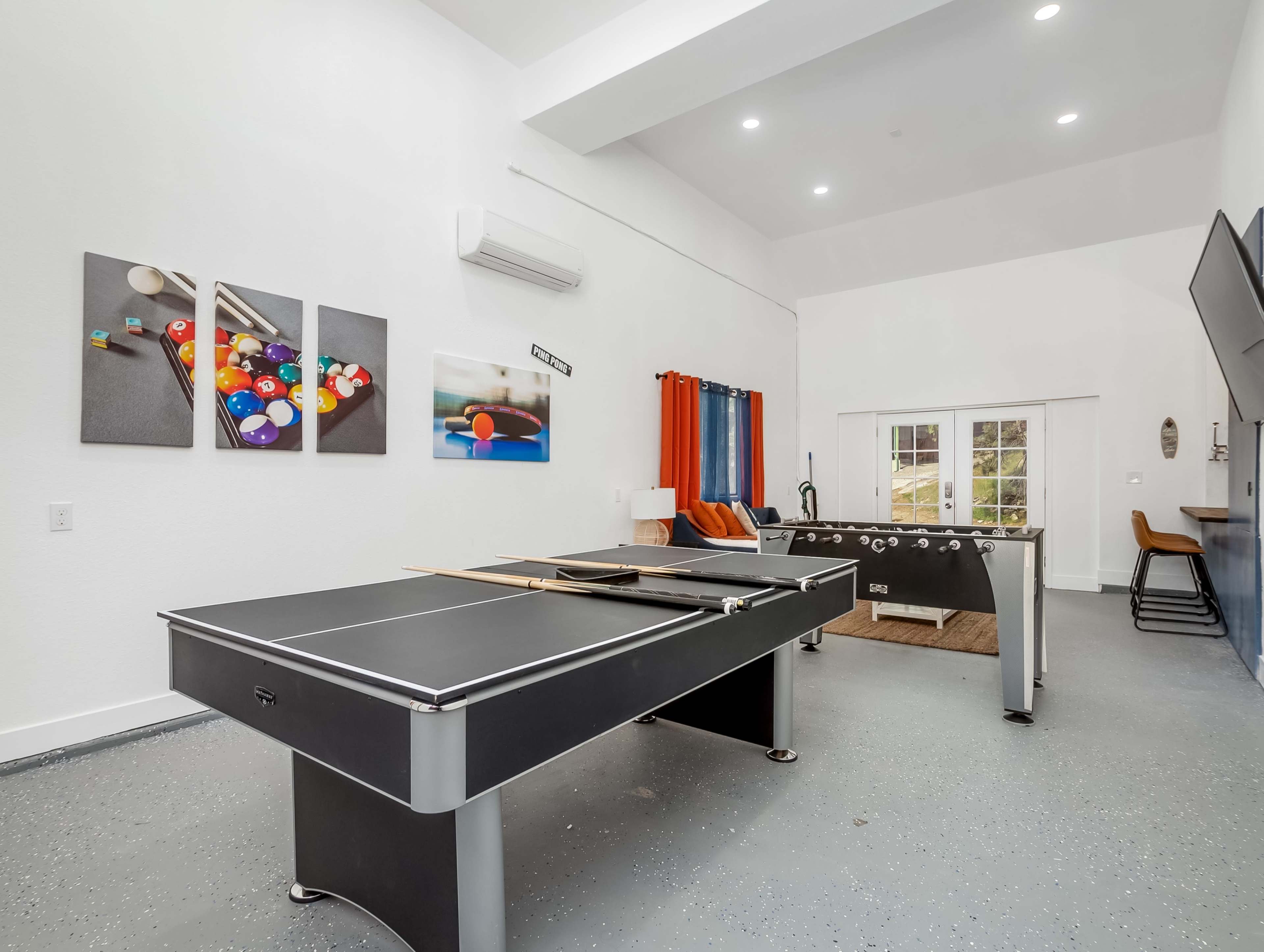 A game room featuring a pool table, a foosball table, and colorful wall art.