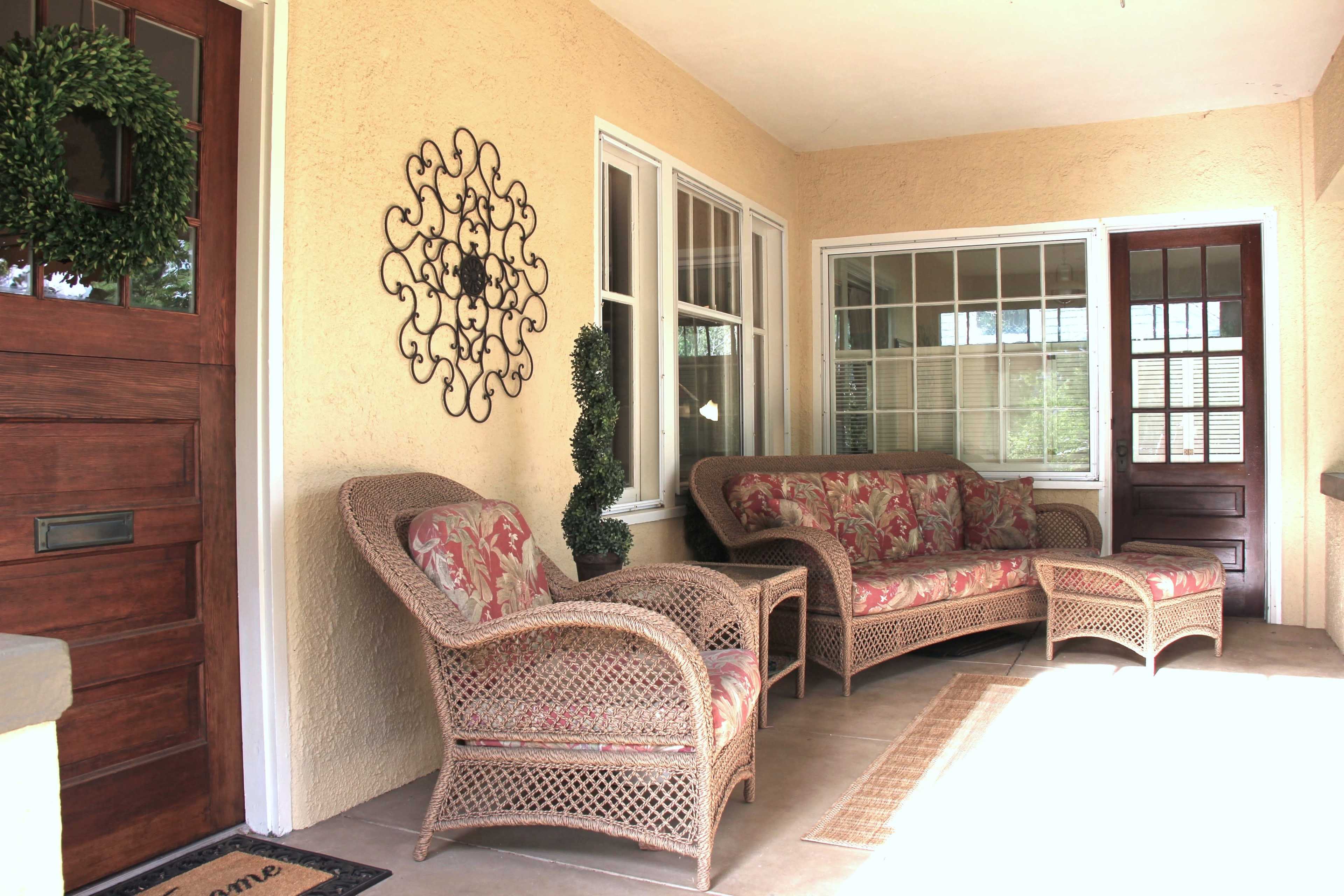 A front porch with a wicker seating area, a small table, and a decorative door with a welcome mat.