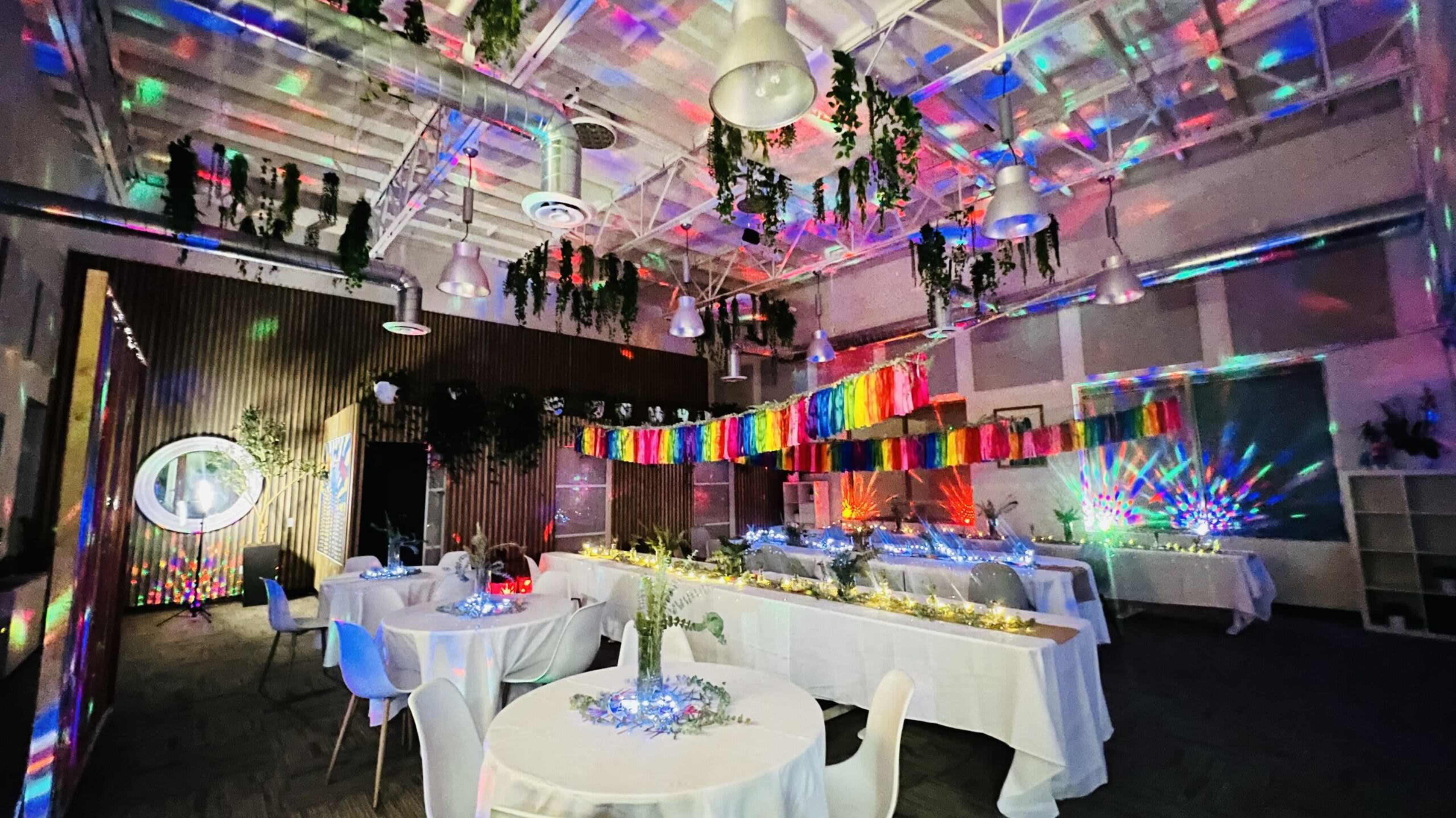 A colorful event space features decorated tables, hanging garlands, and vibrant light projections on the walls and ceiling.