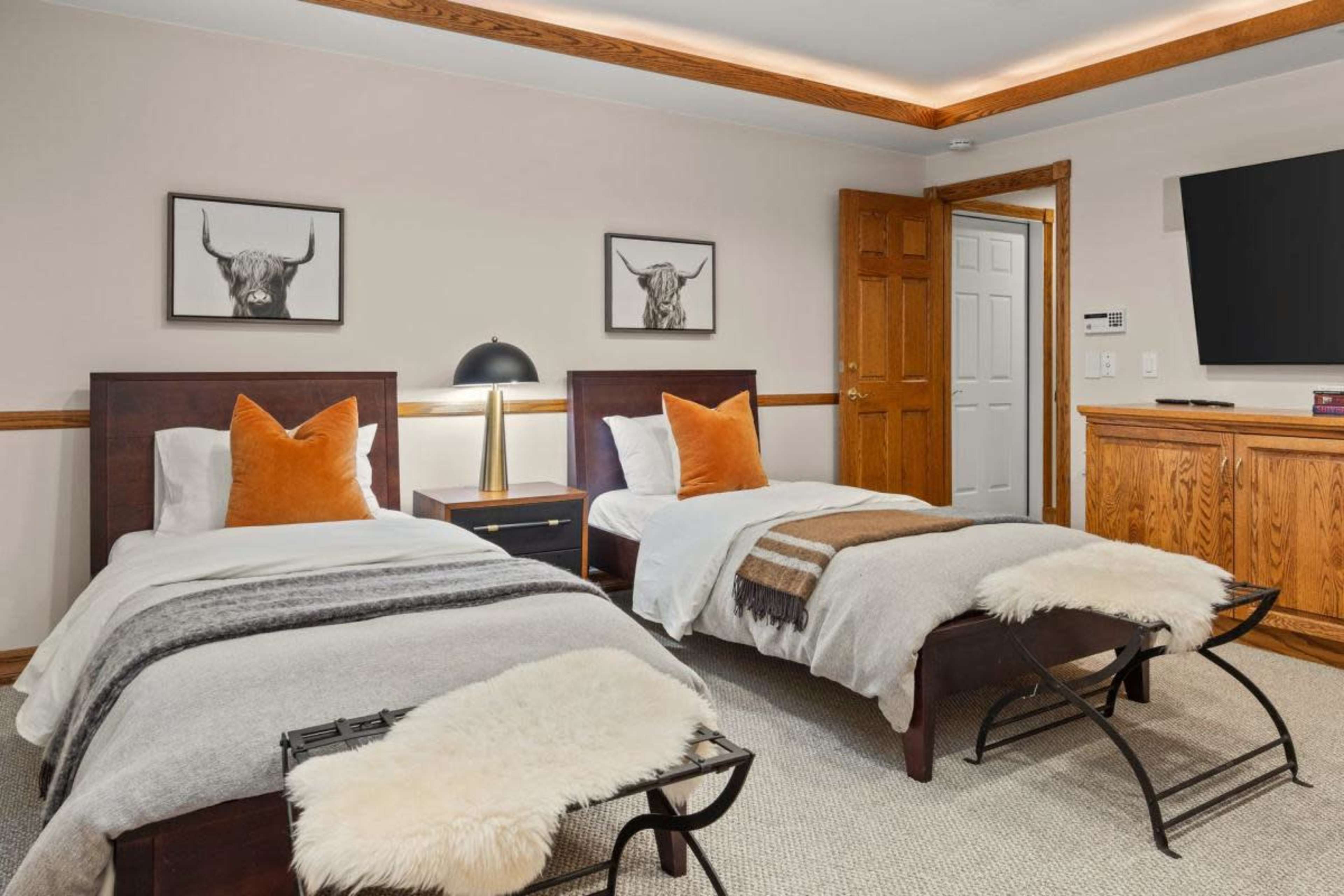 A cozy bedroom featuring two twin beds with orange accent pillows, a bedside table, and wall-mounted artwork of bull head portraits.
