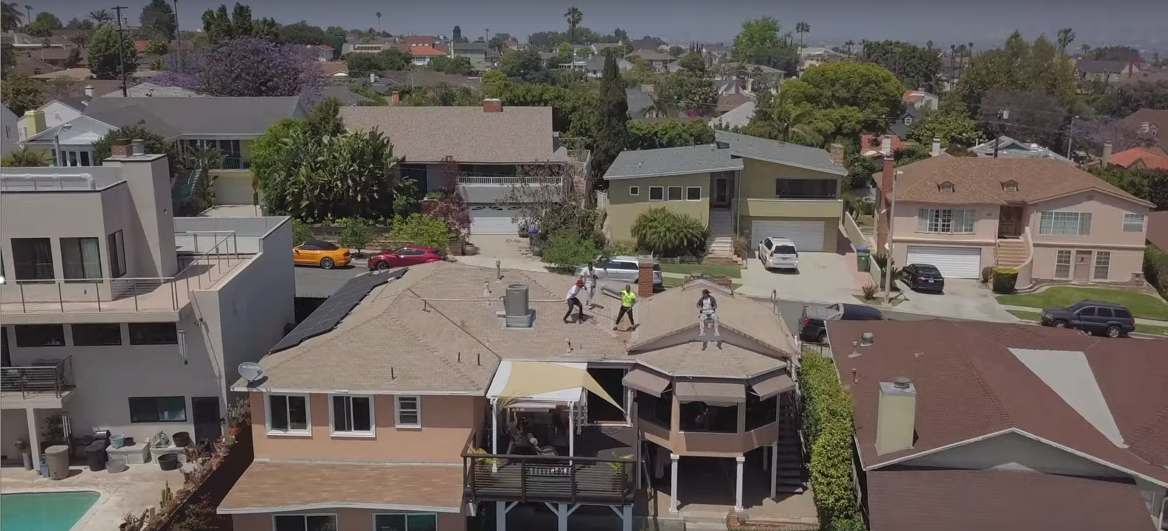 A group of workers is repairing the roof on a house in a suburban neighborhood surrounded by other residential properties.