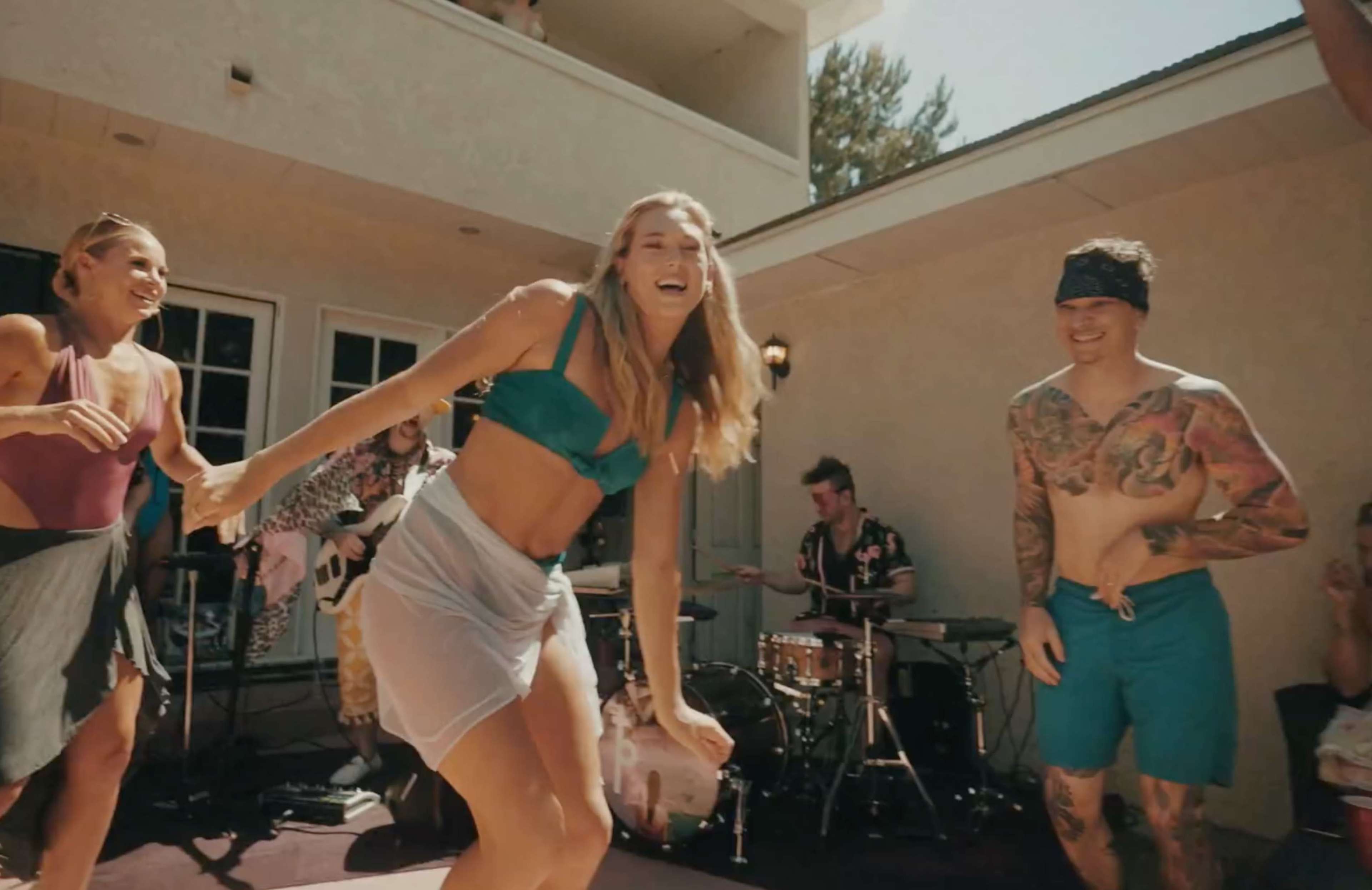 A group of people is dancing and enjoying music outdoors near a house with a band playing in the background.