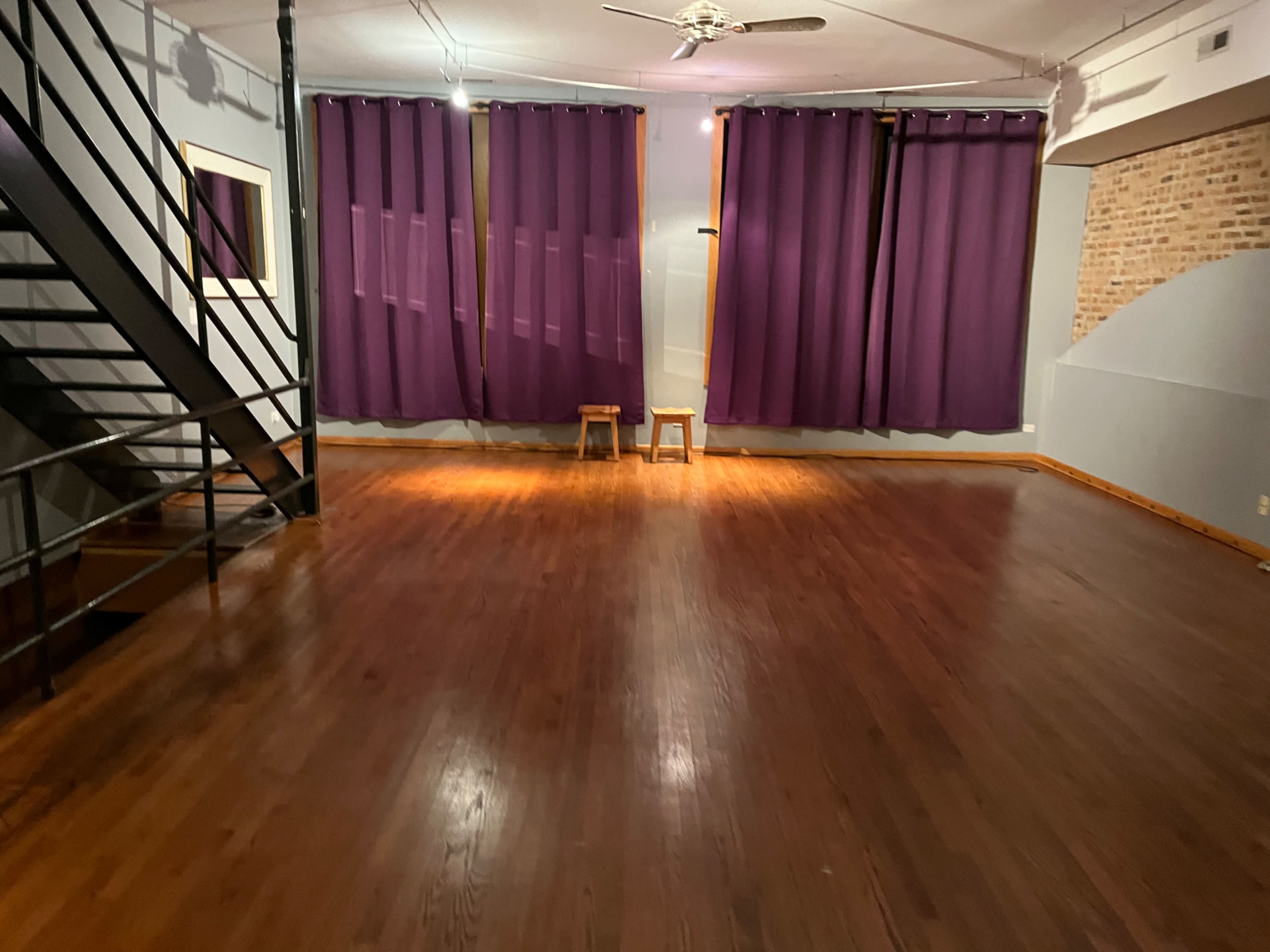 A spacious room with hardwood floors, a staircase, and purple curtains hanging across a window.