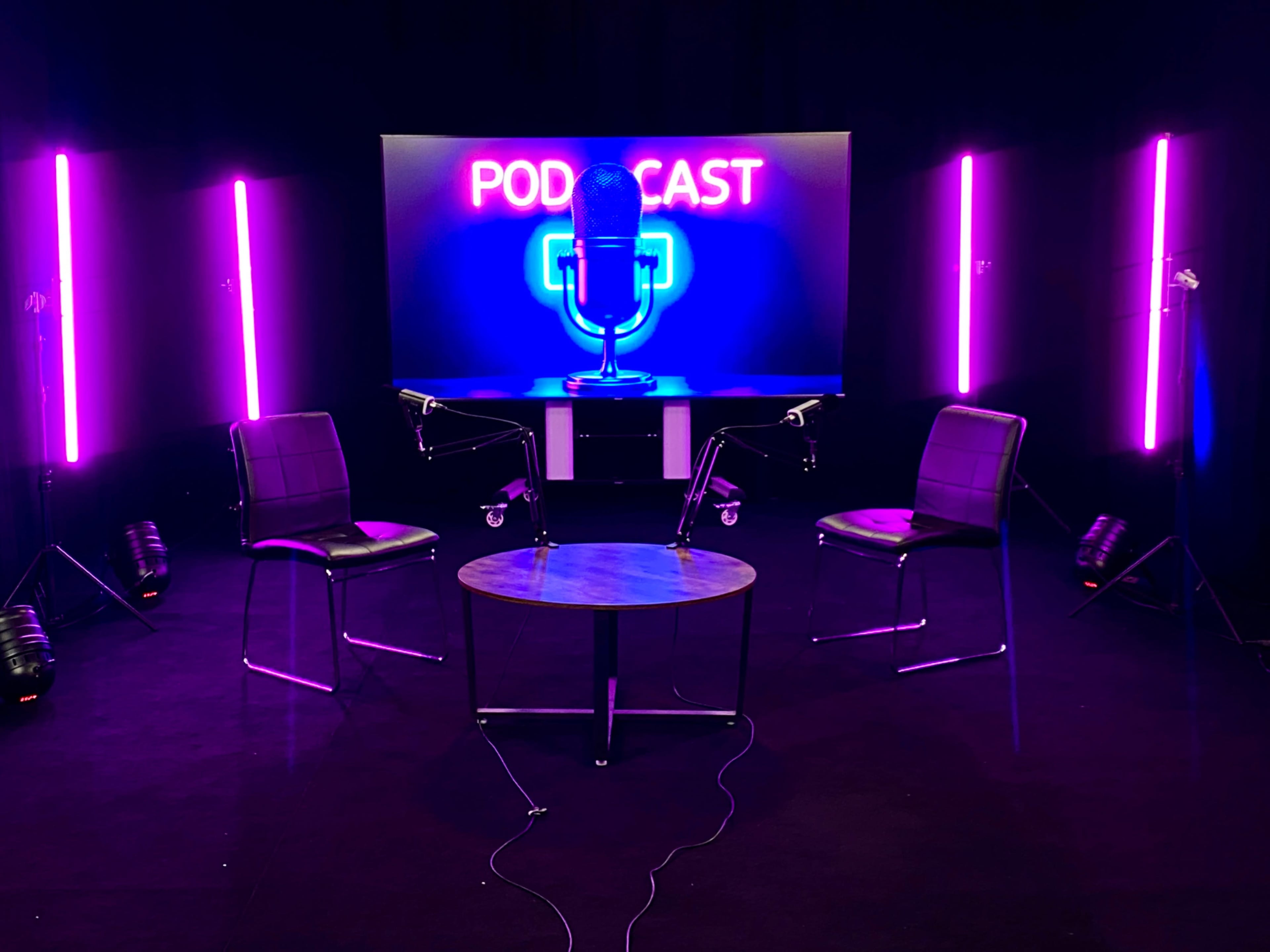 The image features a podcast setup with three chairs and a table, illuminated by neon pink lights and a backdrop displaying the word "PODCAST" with a microphone graphic.