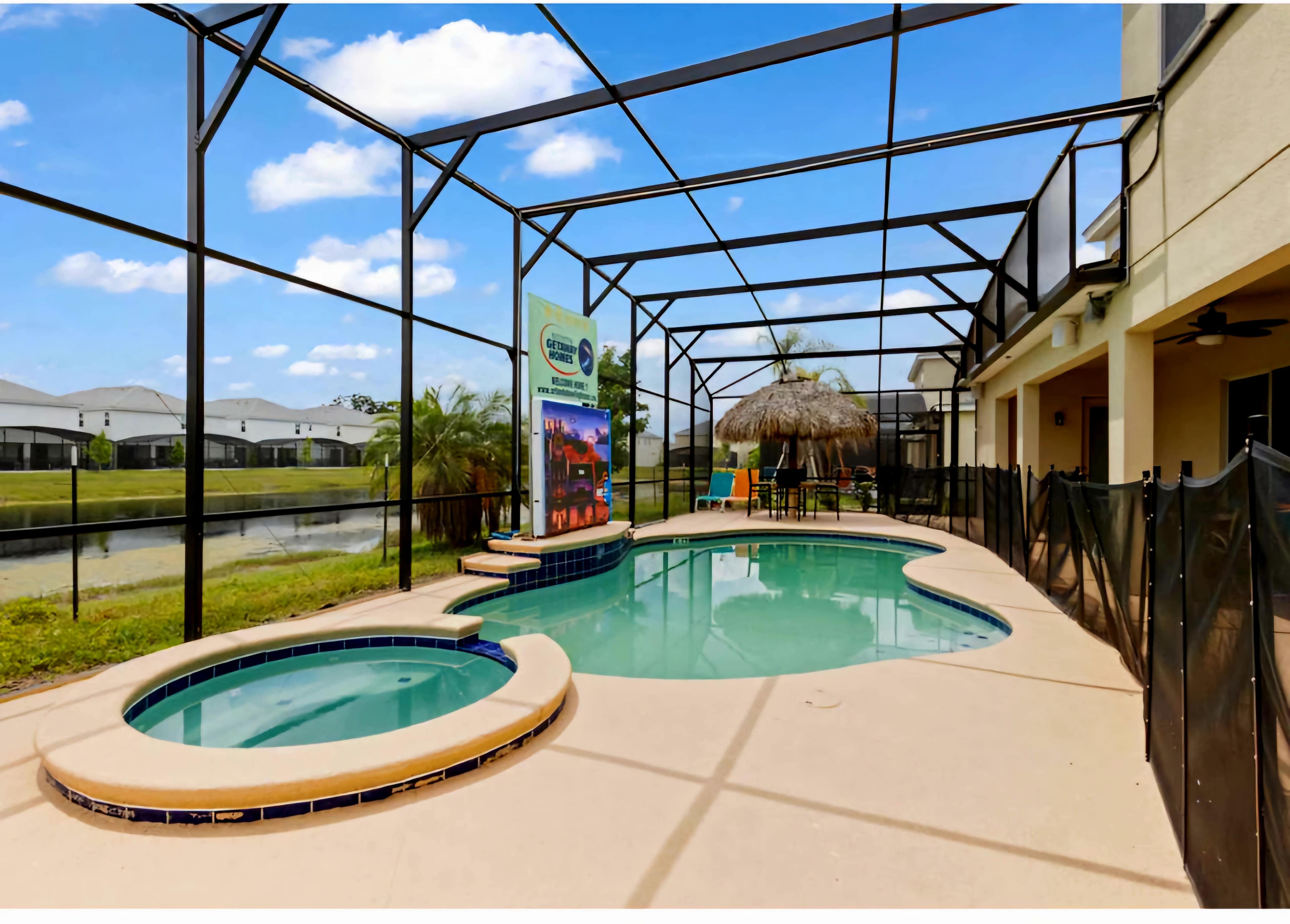 A screened-in patio featuring a swimming pool, a spa, and a thatched umbrella, with residential homes visible in the background.