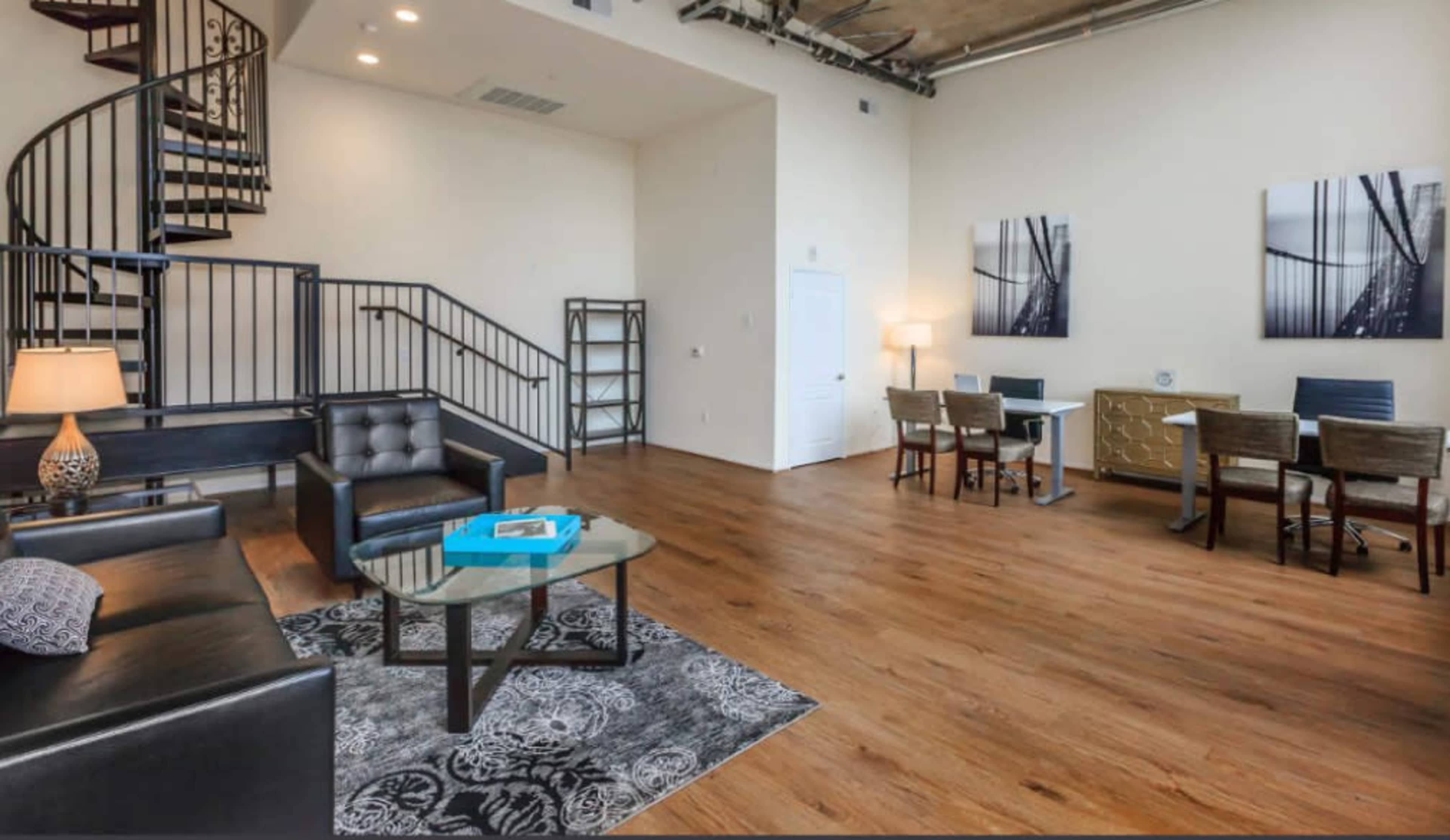 The image shows a modern living space featuring a spiral staircase, a seating area with a coffee table, and a dining area with a table and chairs.