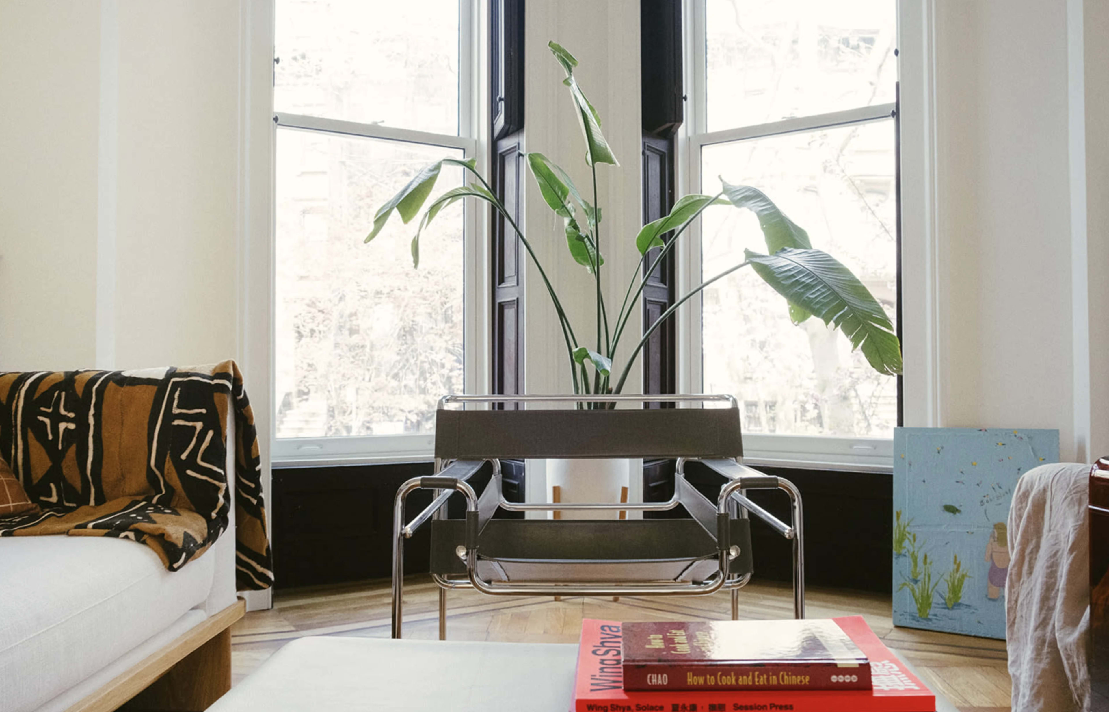 A chair with a metal frame and a potted plant sits in front of a large window in a well-lit room.