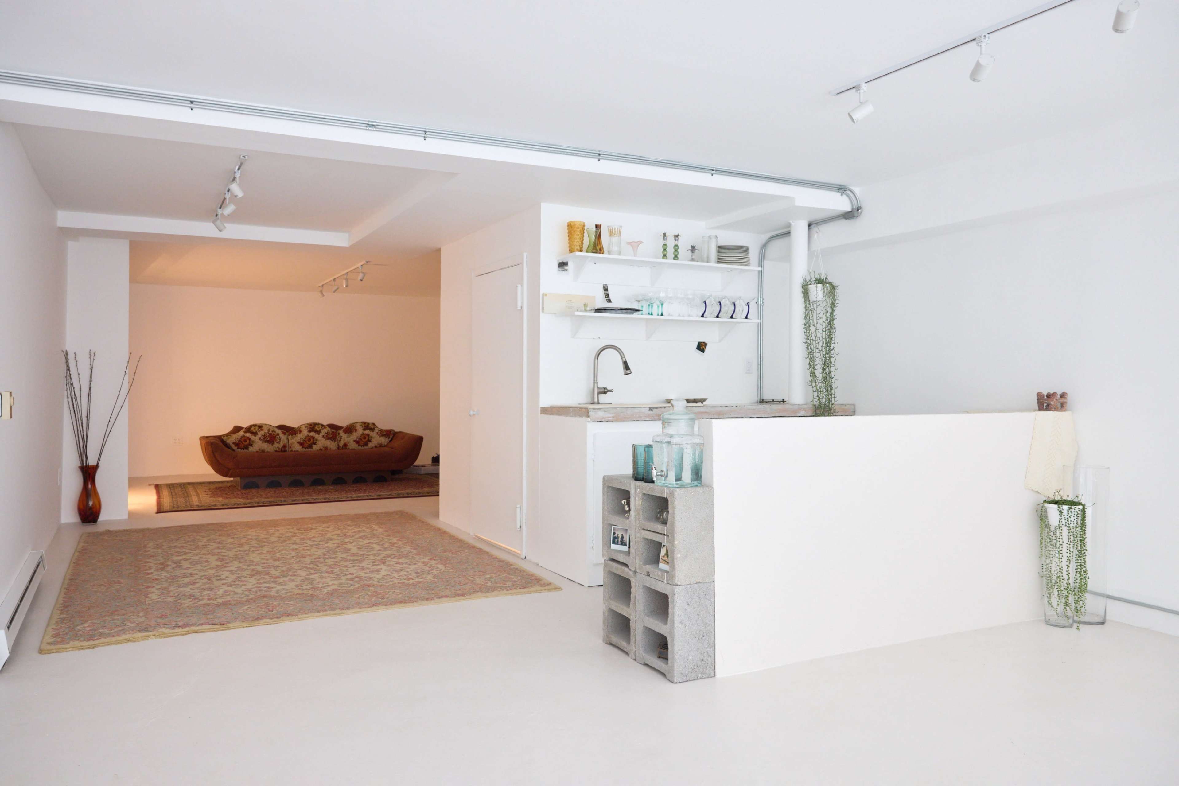 A spacious, modern interior with a bar-like counter made of concrete blocks, leading to a living area with a patterned rug and a sofa.
