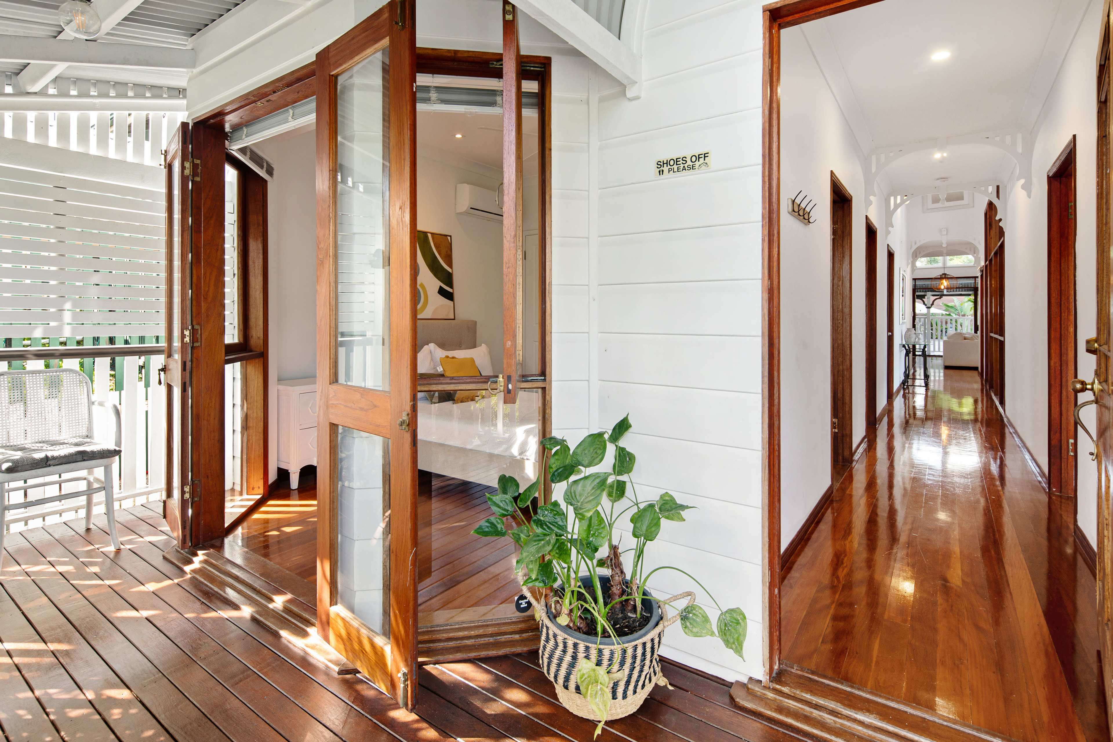 A hallway with polished wooden floors and large sliding glass doors opens to a cozy room, with green plants in a pot near the entrance.