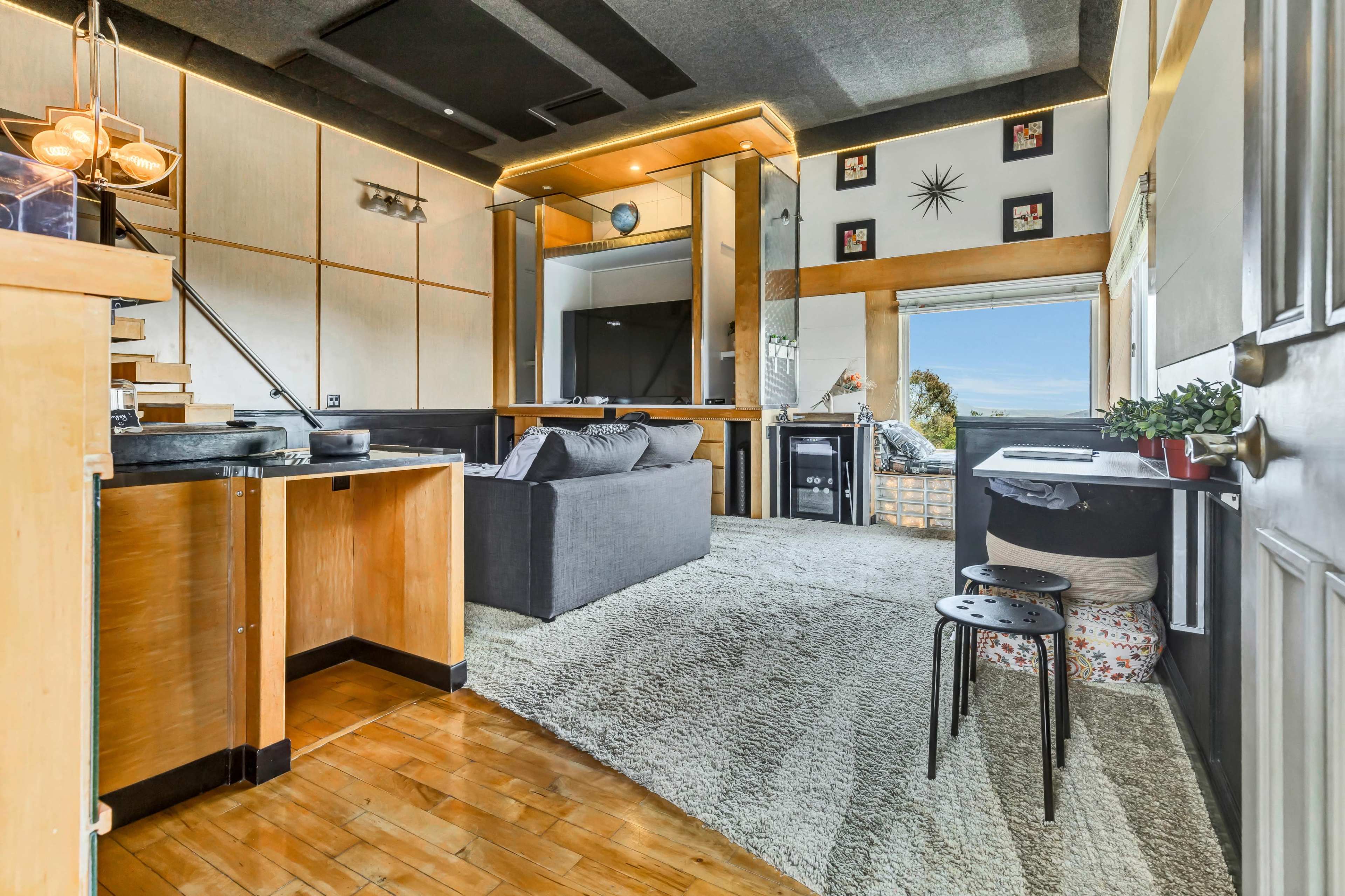 A modern living area with a gray sofa, wooden accents, and large windows offering a view.
