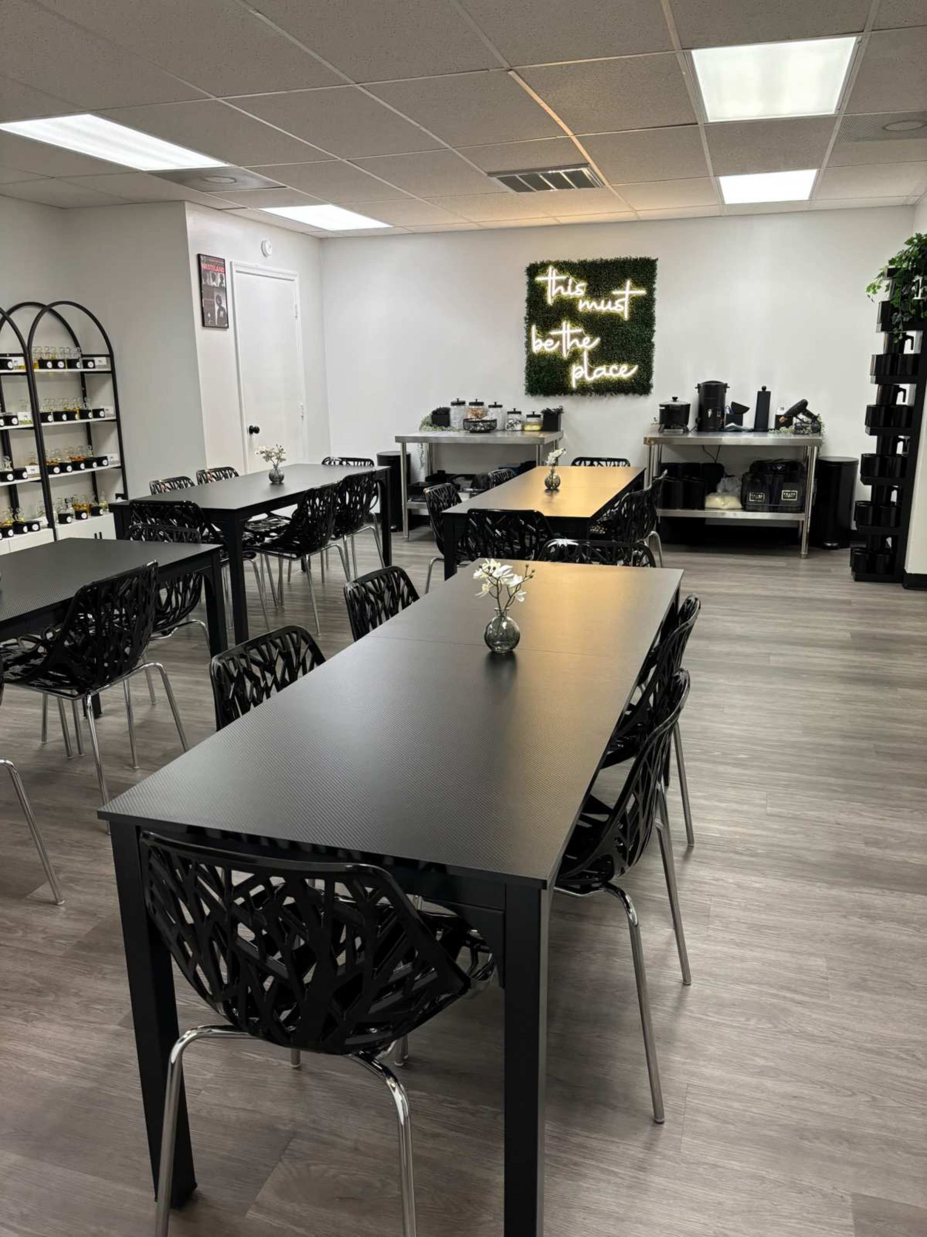 A modern, well-lit meeting room with black tables and chairs, featuring a decorative wall with the phrase "This must be the place" and a small flower arrangement on each table.