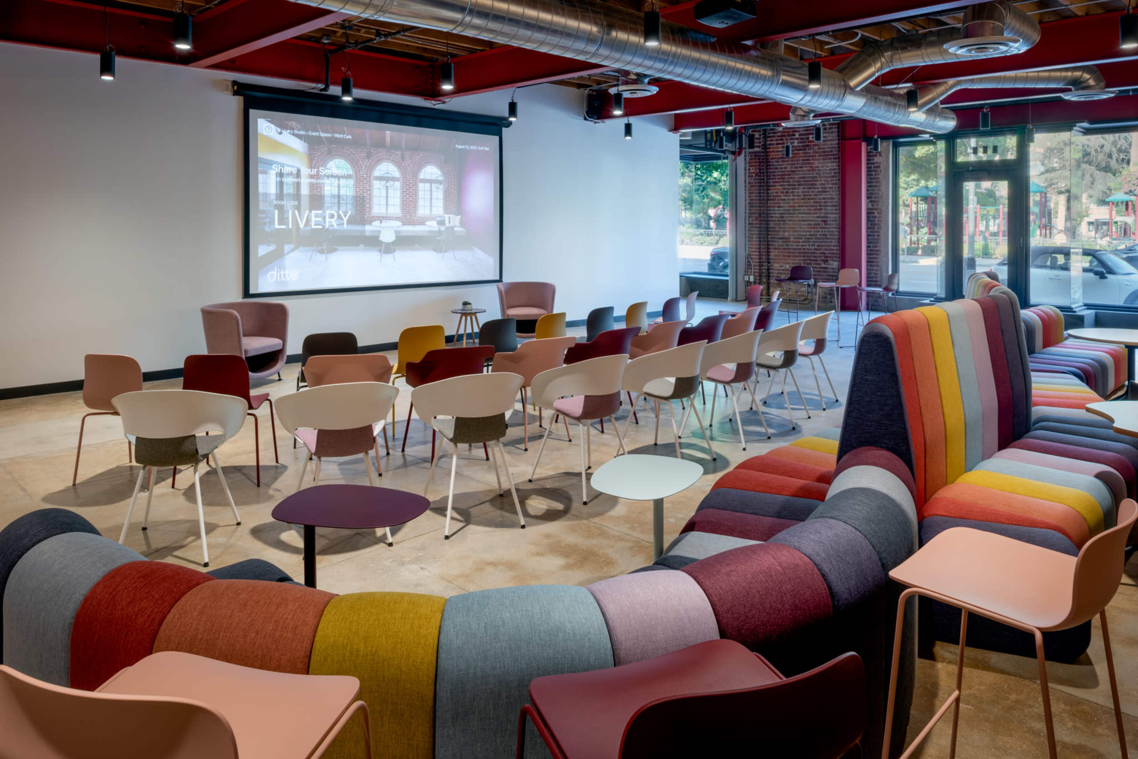 A modern meeting room with colorful seating arrangements and a large screen at the front.