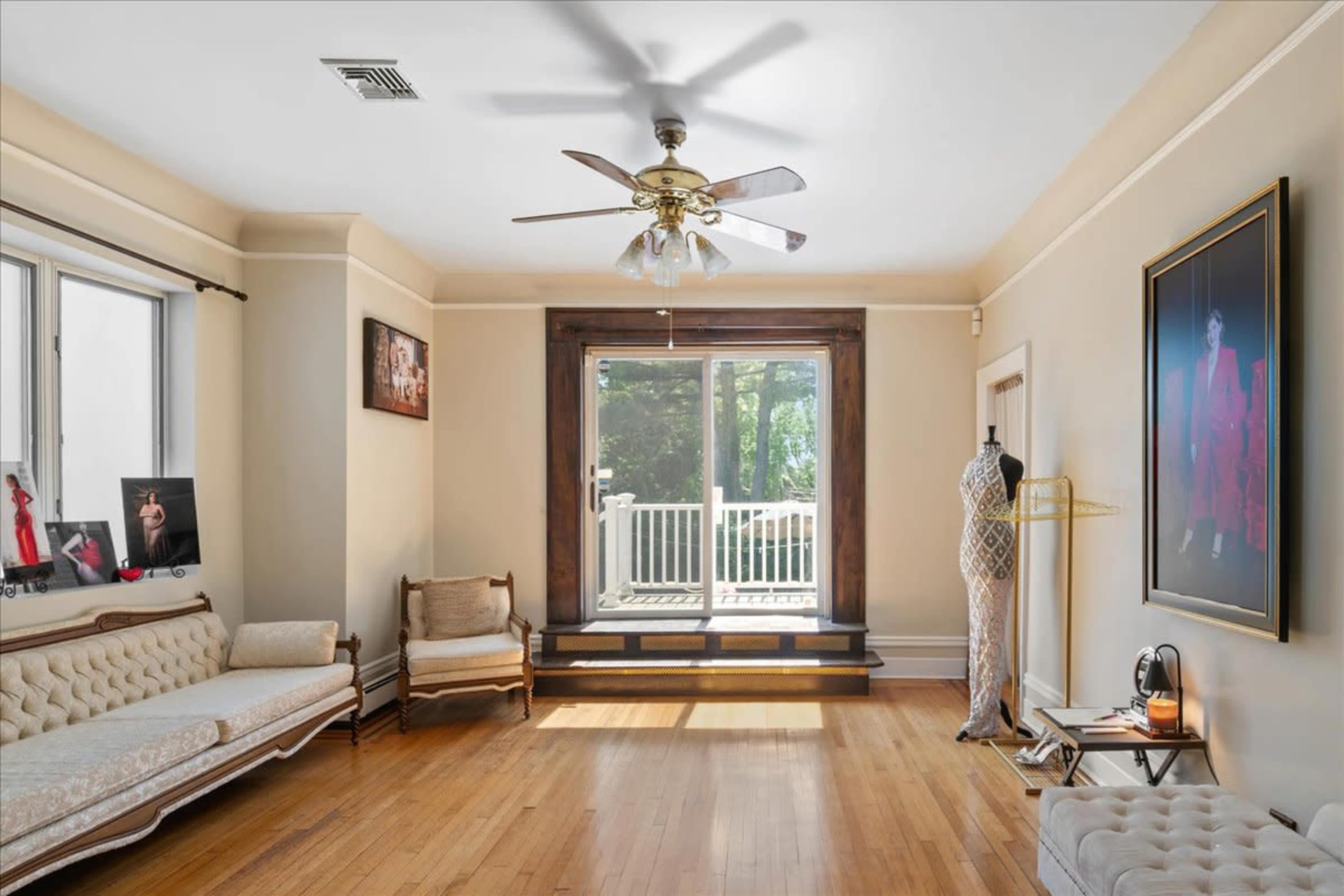 A brightly lit living room features a wooden floor, a sliding glass door leading to a porch, and various pieces of furniture including a sofa and a mannequin.