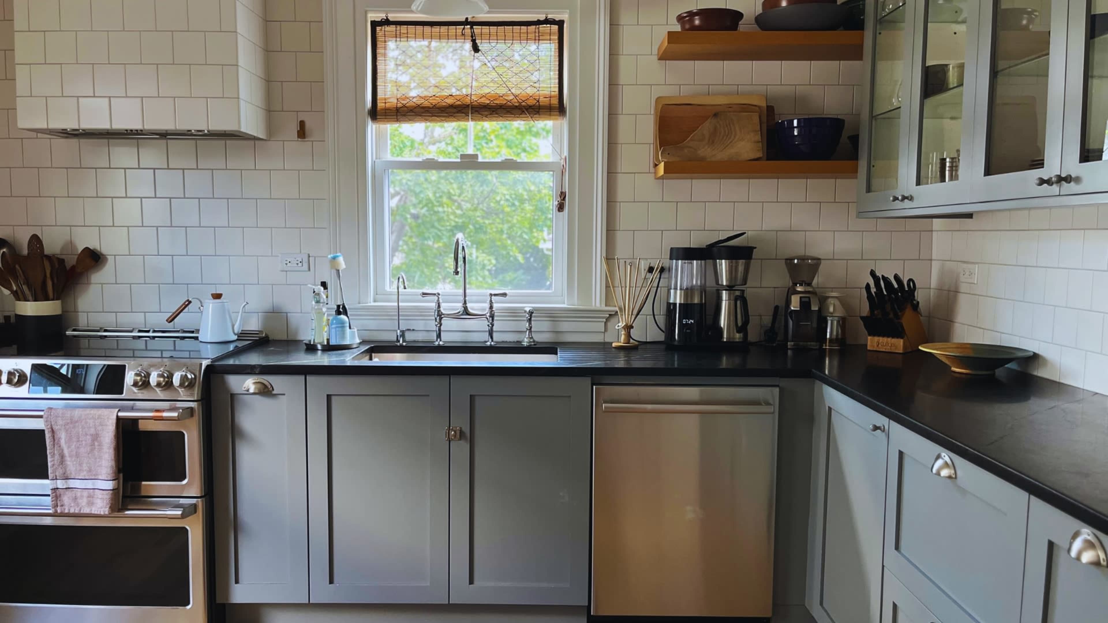 The image shows a modern kitchen featuring gray cabinetry, stainless steel appliances, and a window with natural light.