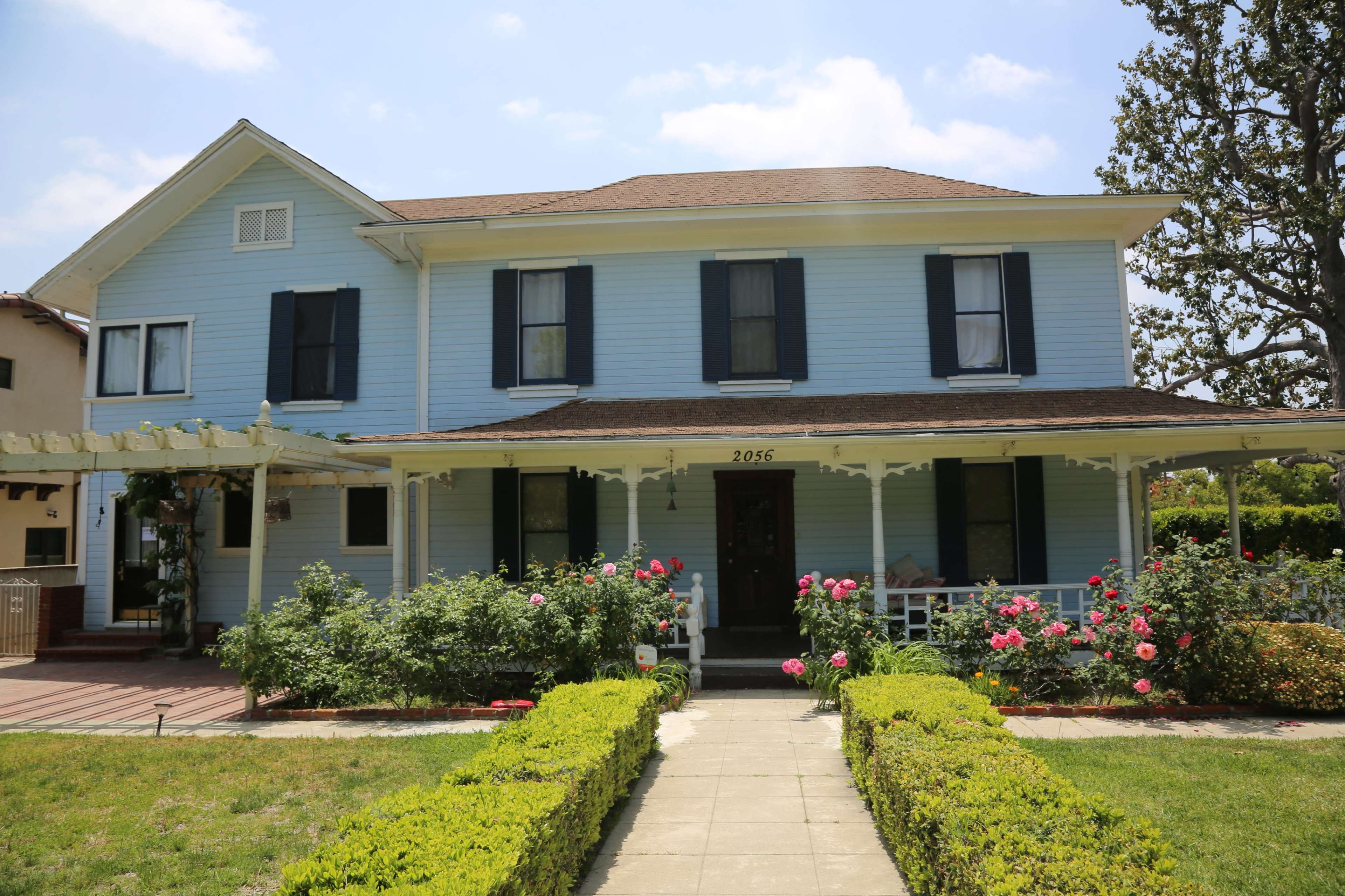 A light blue two-story house with black shutters surrounded by flower beds and a well-maintained lawn.