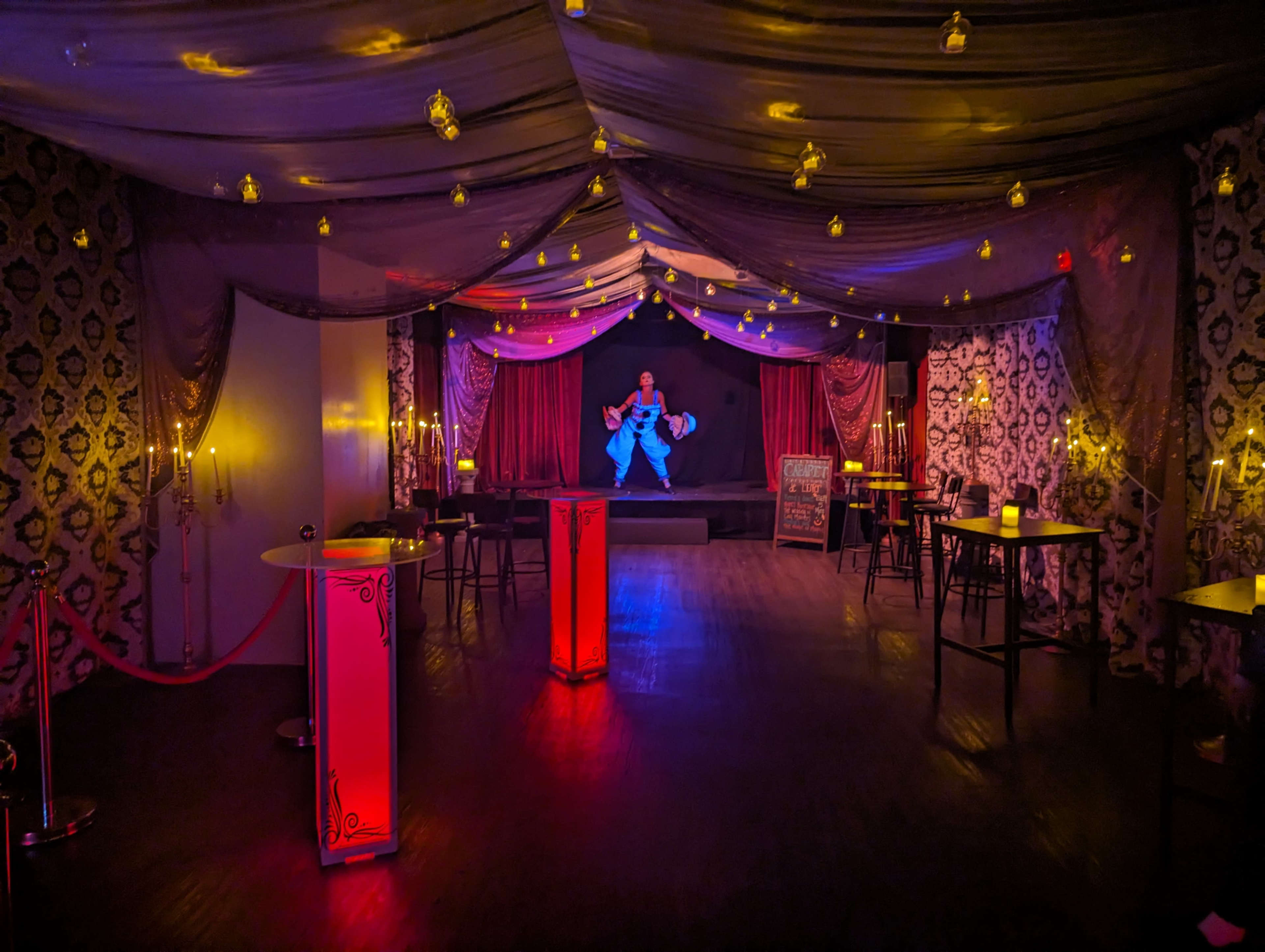 A performer dressed in a blue outfit stands on a stage under dim lighting in a decorated event space.
